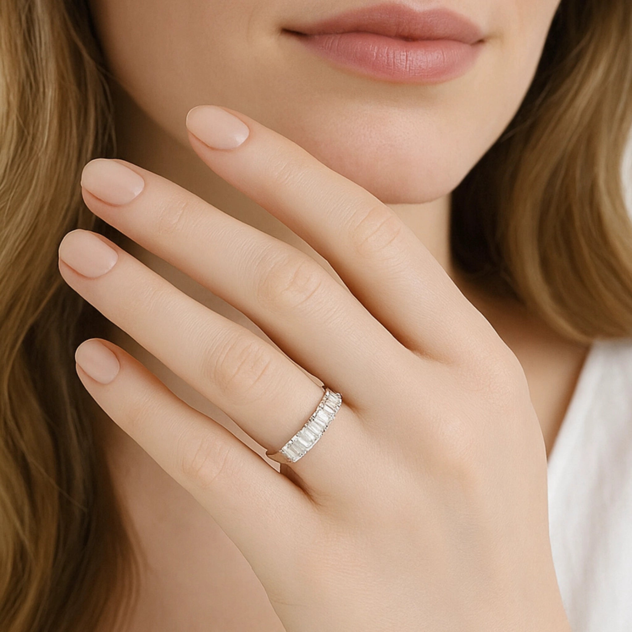 Close-up of a woman's hand wearing a seven stone emerald cut diamond eternity ring, showcasing elegance and sparkle.