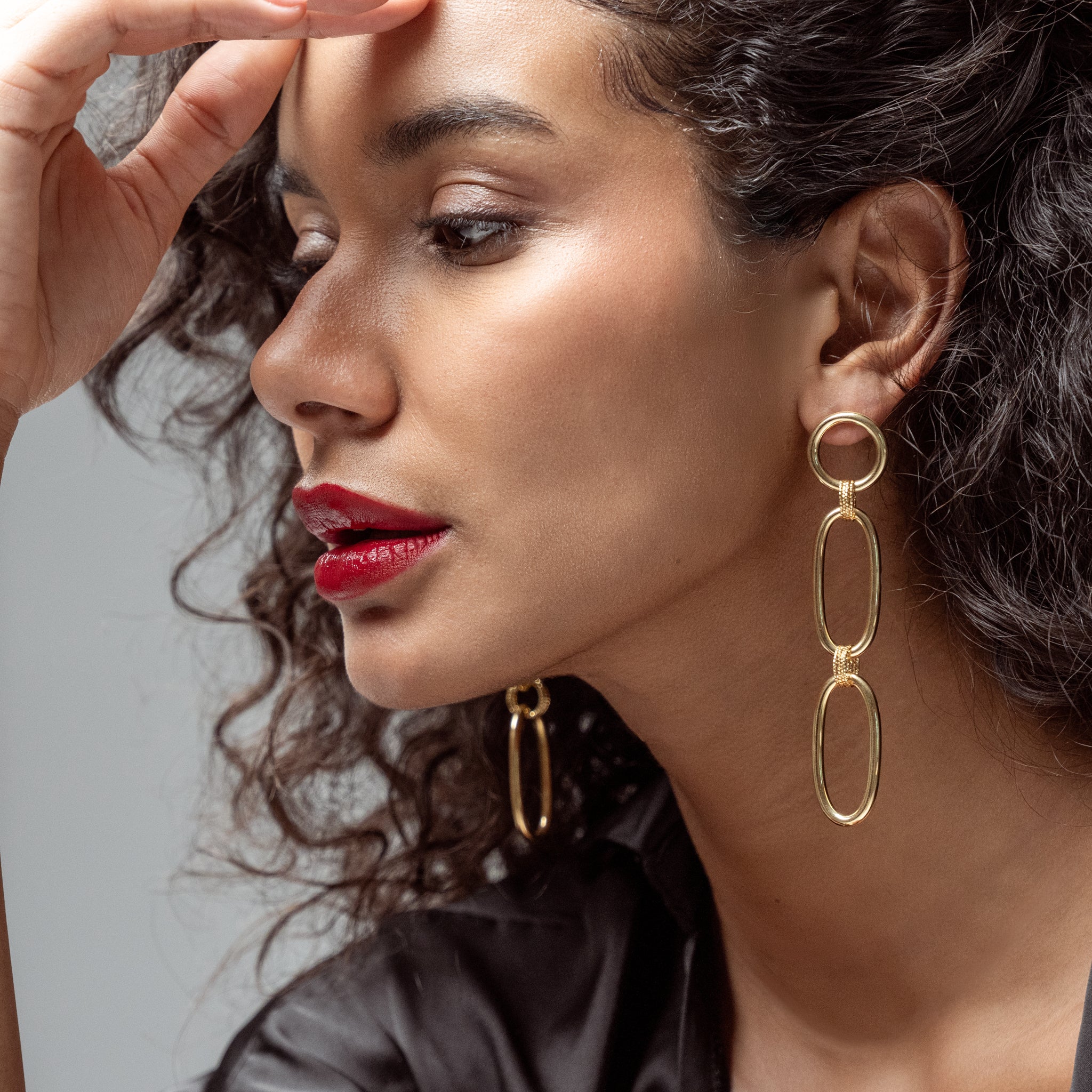 Close-up of a woman wearing yellow gold chain earrings with a neutral background