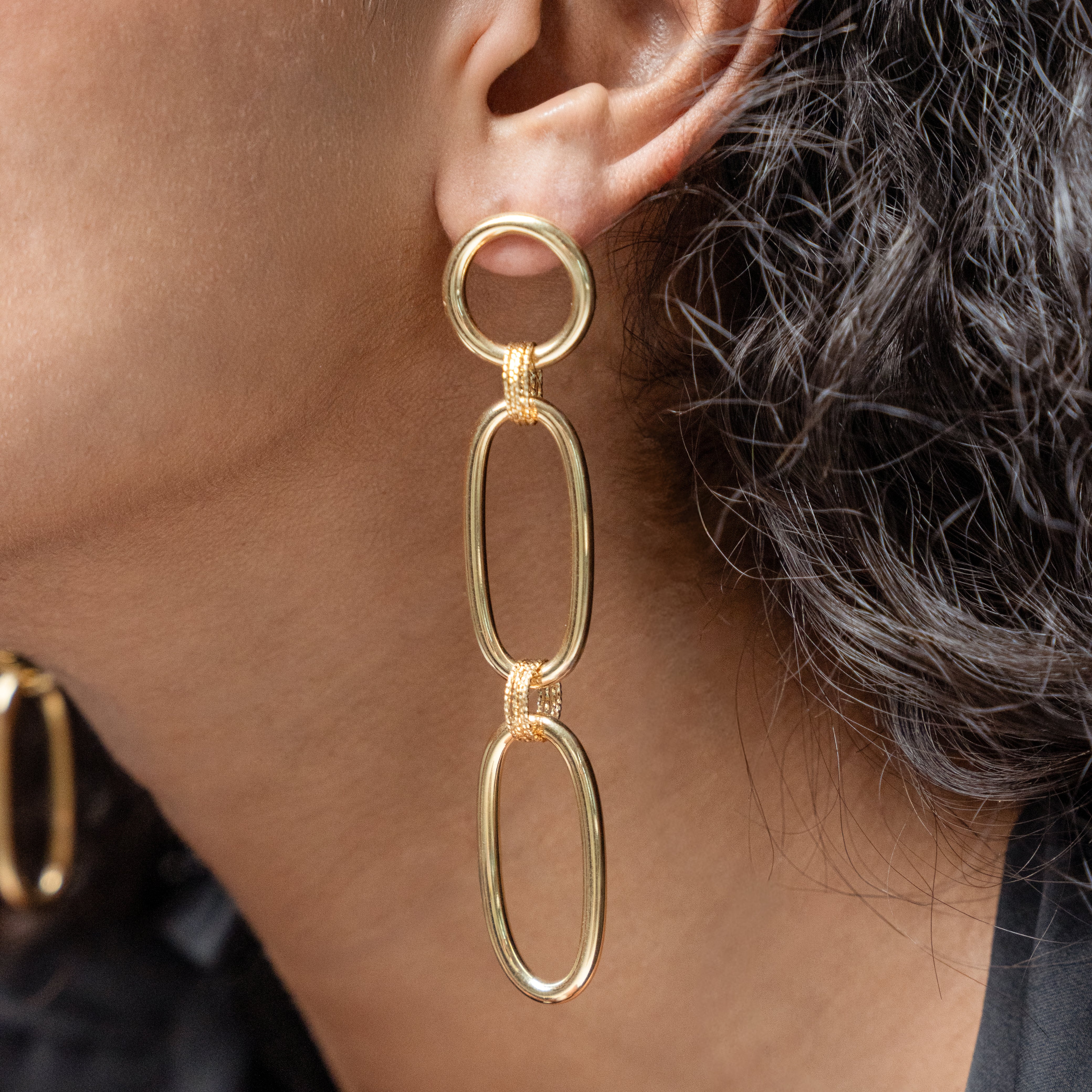 Gold chain earrings worn by a person with dark hair.