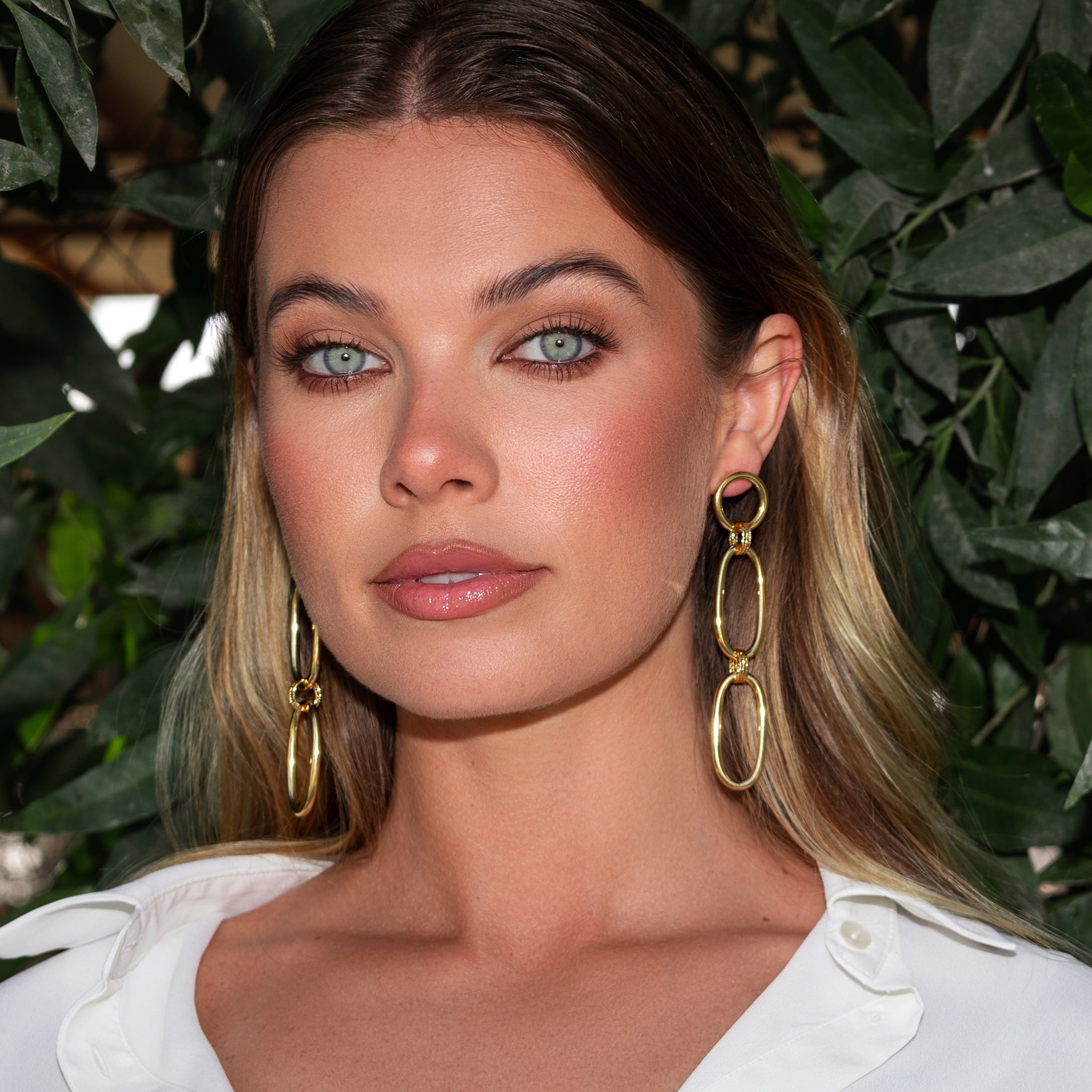 Woman wearing gold hoop earrings with a green leafy background