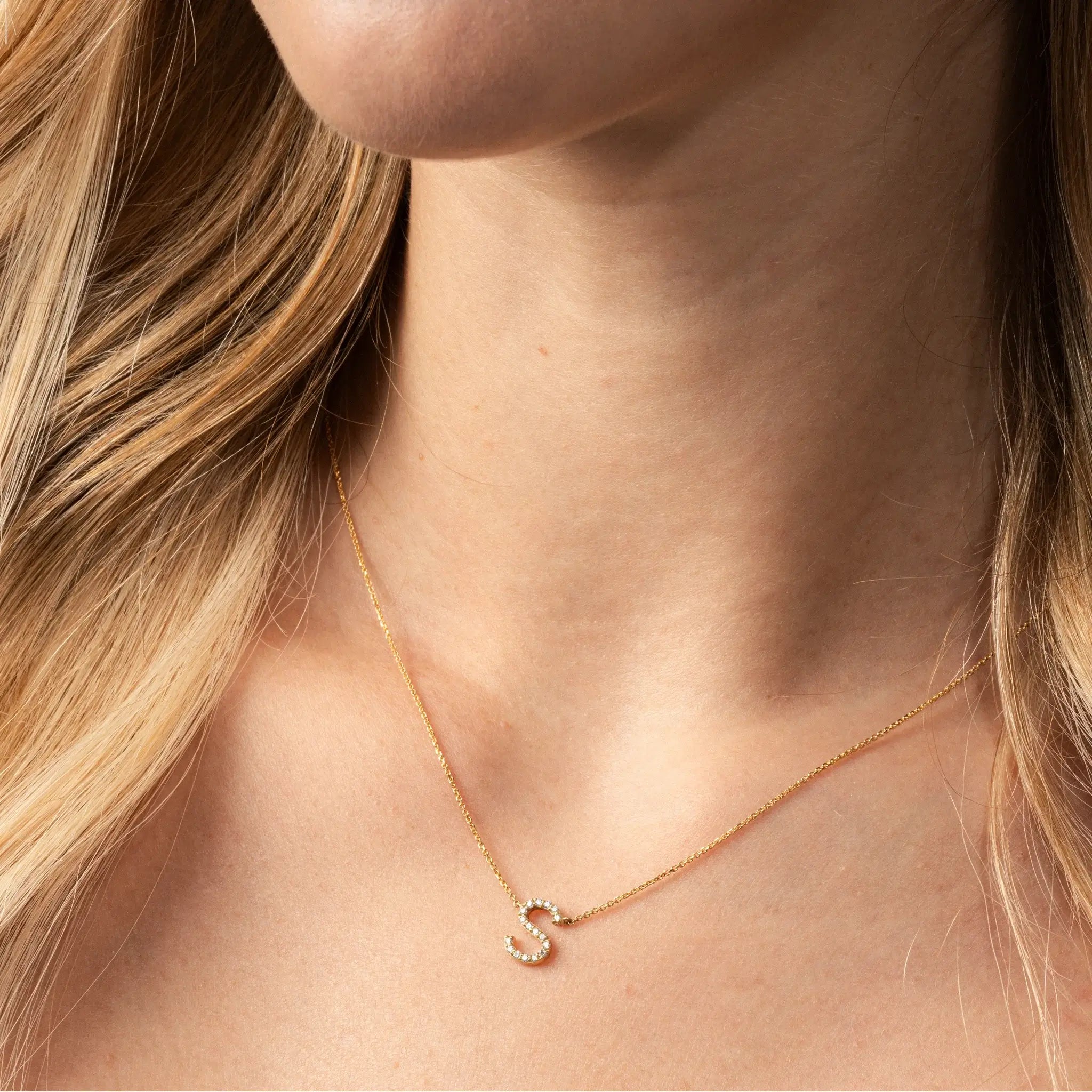 Gold diamond necklace with a 'S' pendant on a person's neck