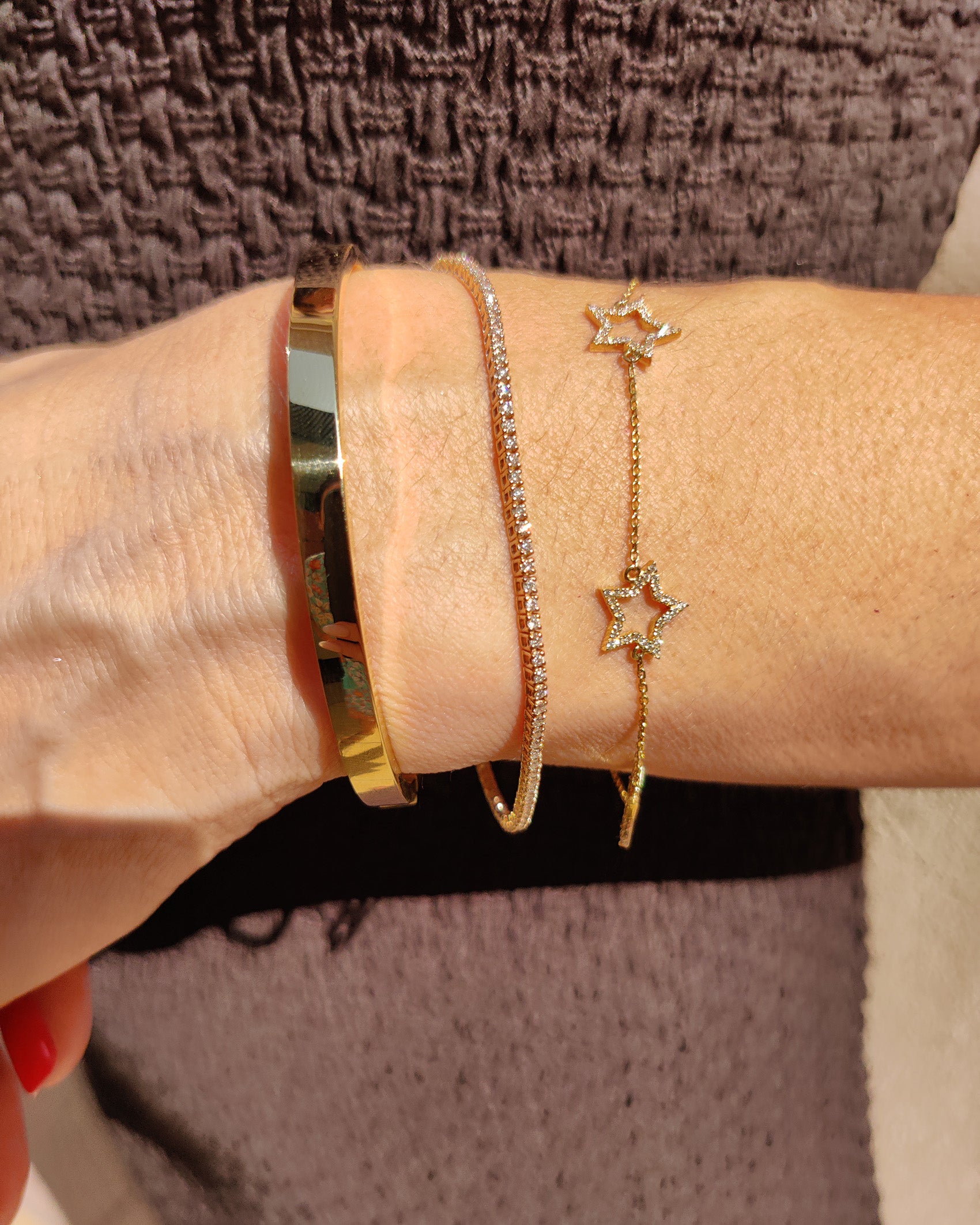 Close-up of a hand wearing a diamond star bracelet on a delicate chain with a golden cuff and sparkly bangle.