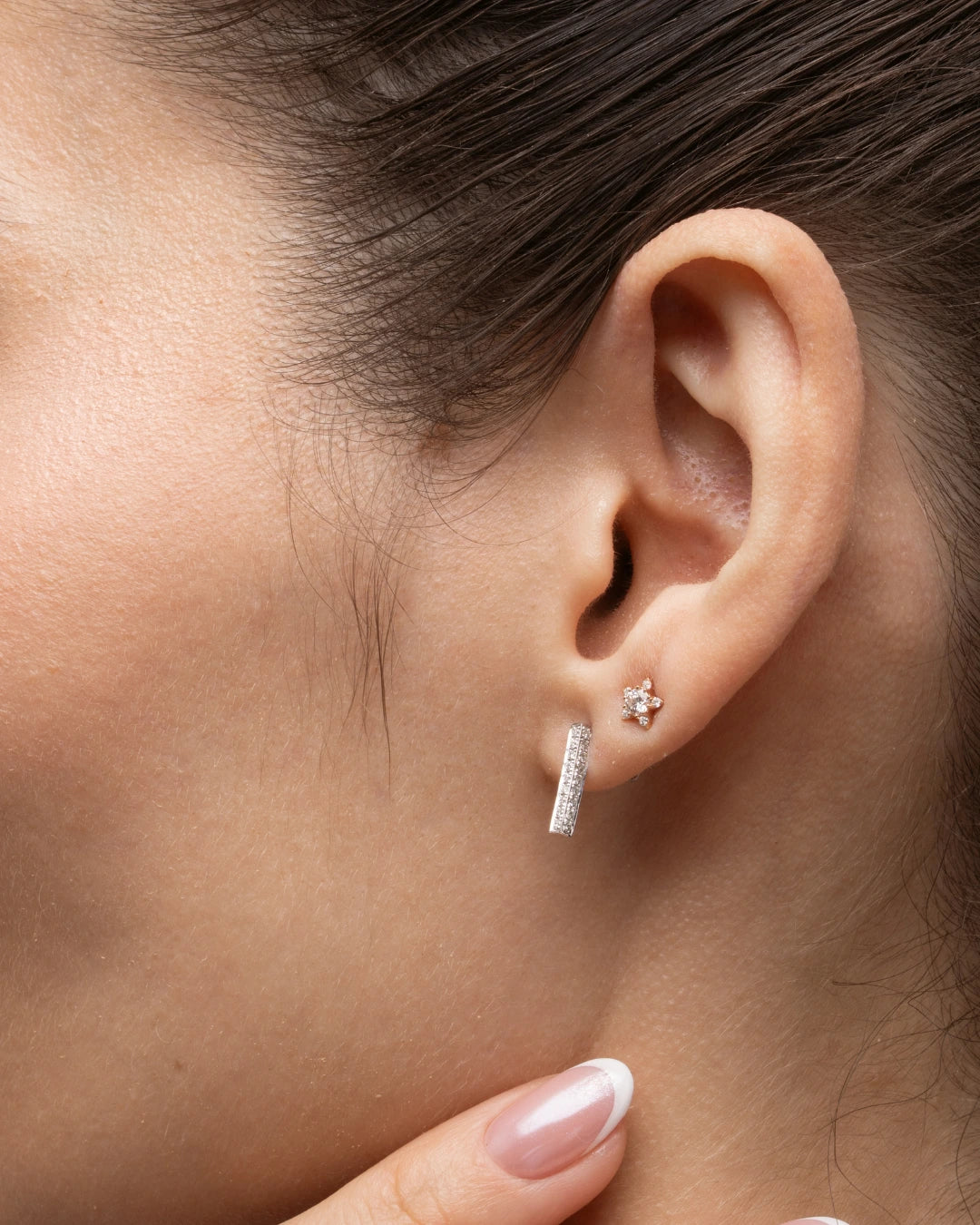 Model showcasing certified diamond earrings in gold bar style alongside a floral stud earring.