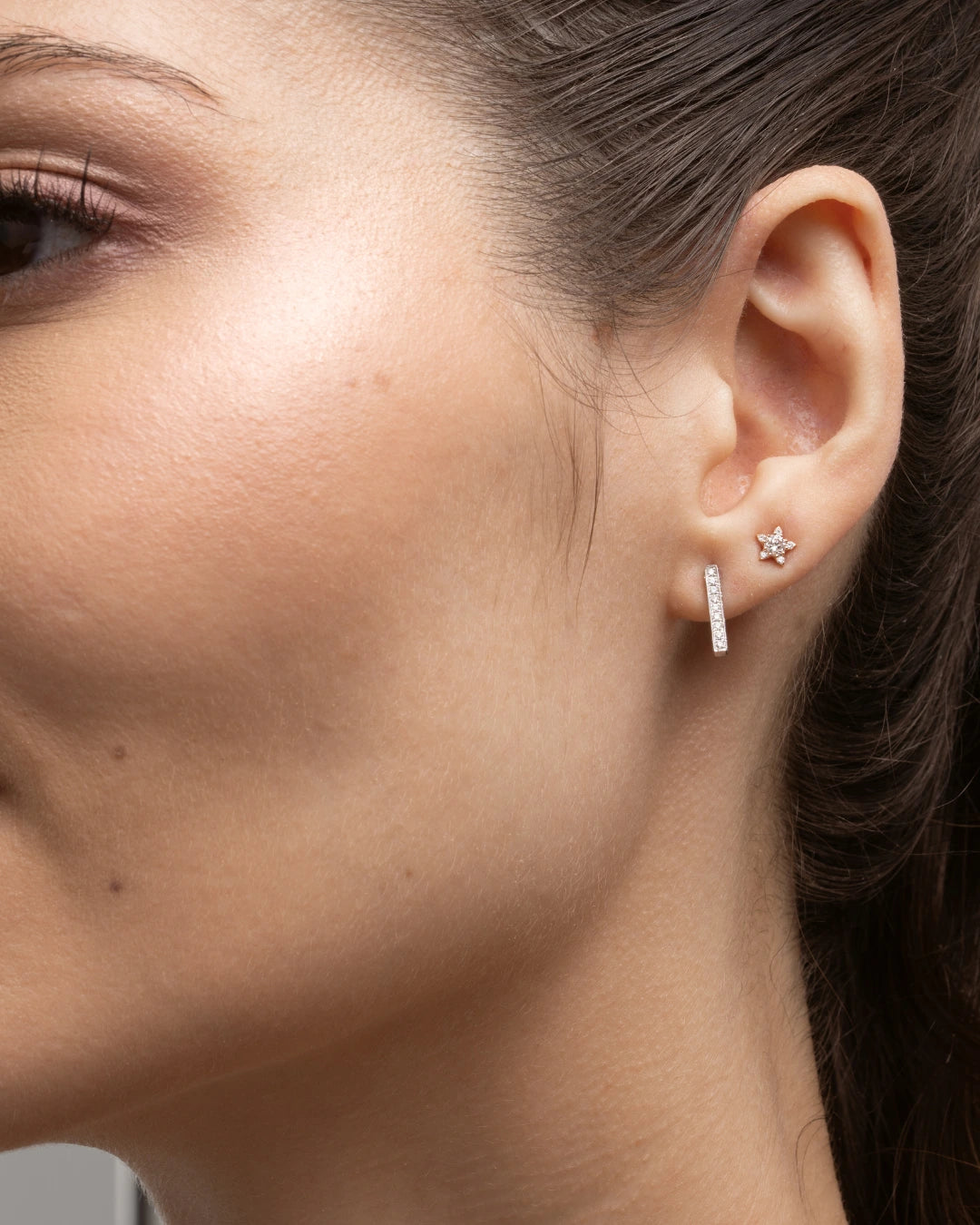 Close-up of a woman's ear featuring certified diamond earrings, showcasing a star design with sparkling diamonds.