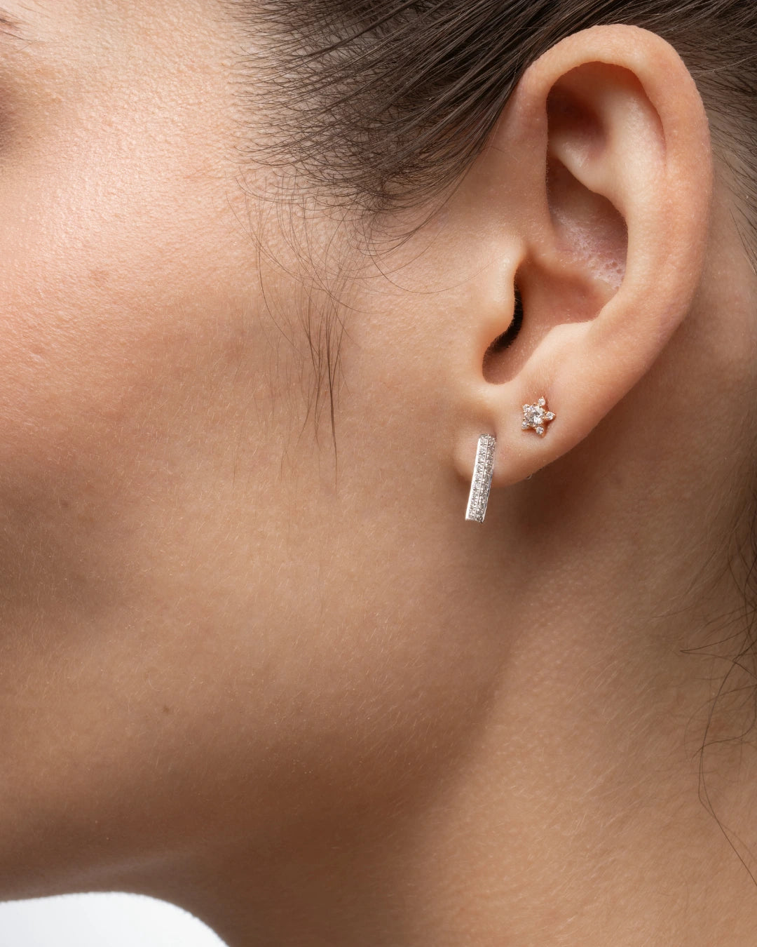 Close-up of a woman's ear adorned with small star earrings featuring certified diamond accents.