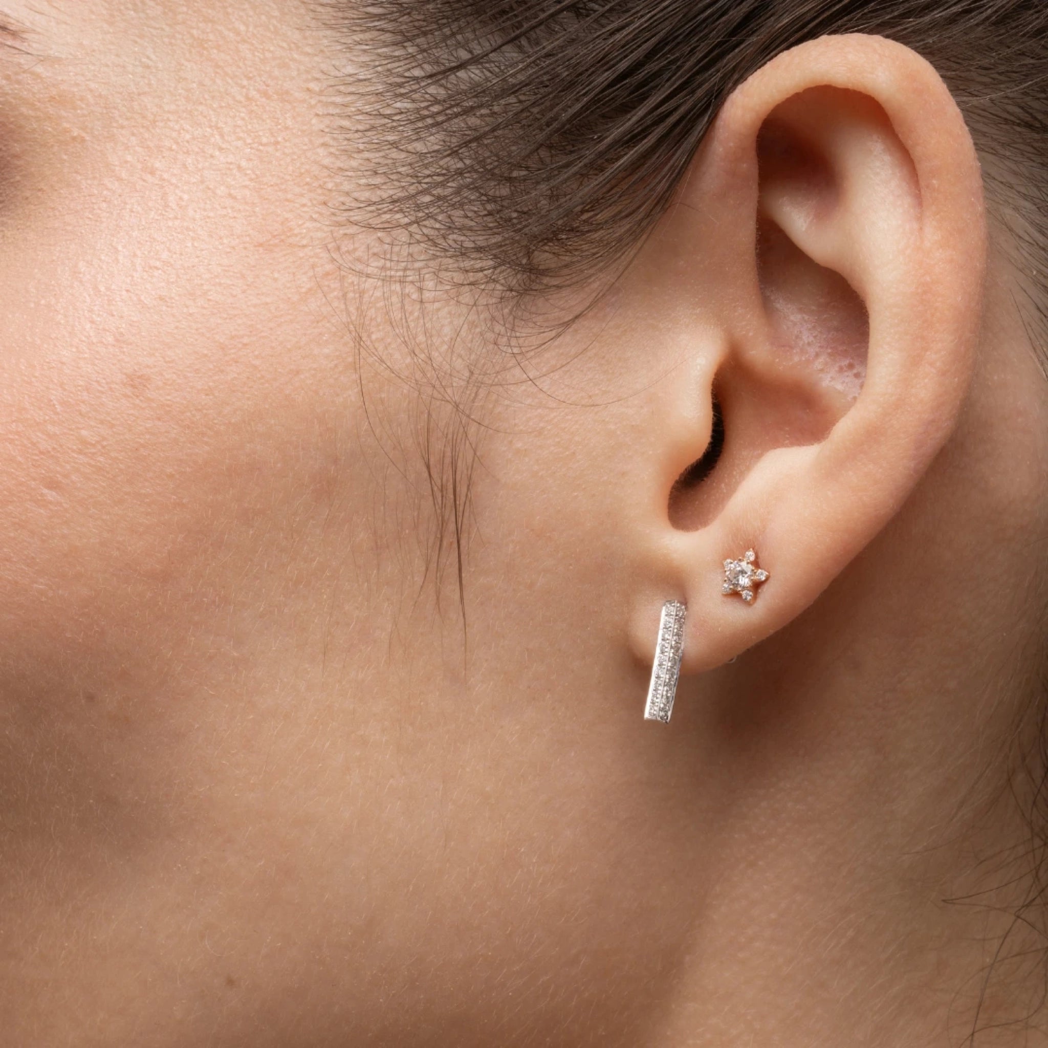 Close-up of a woman's ear adorned with small star earrings featuring certified diamond accents.
