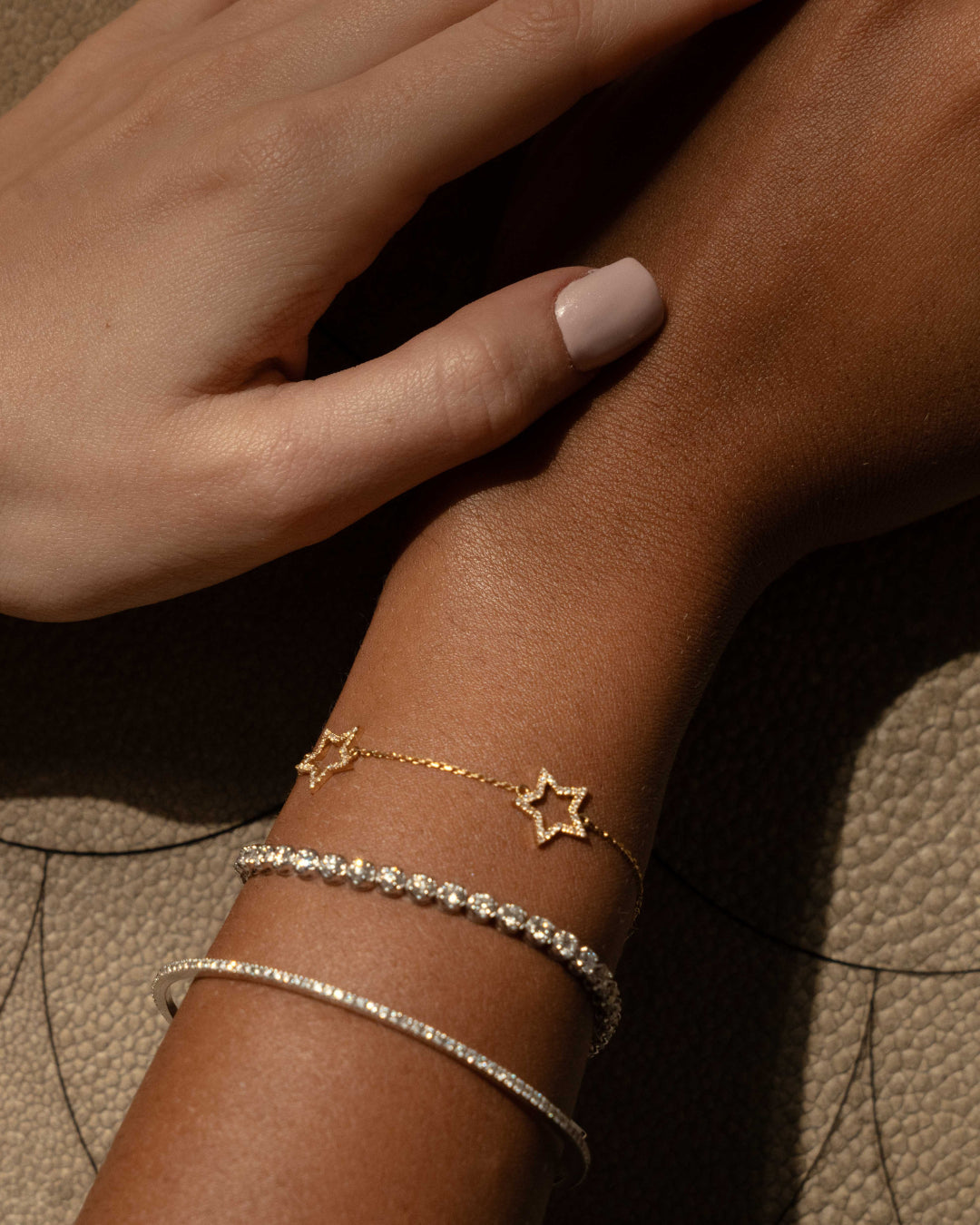 Close-up of a hand wearing a star diamond bracelet alongside two elegant bangles on a textured surface.