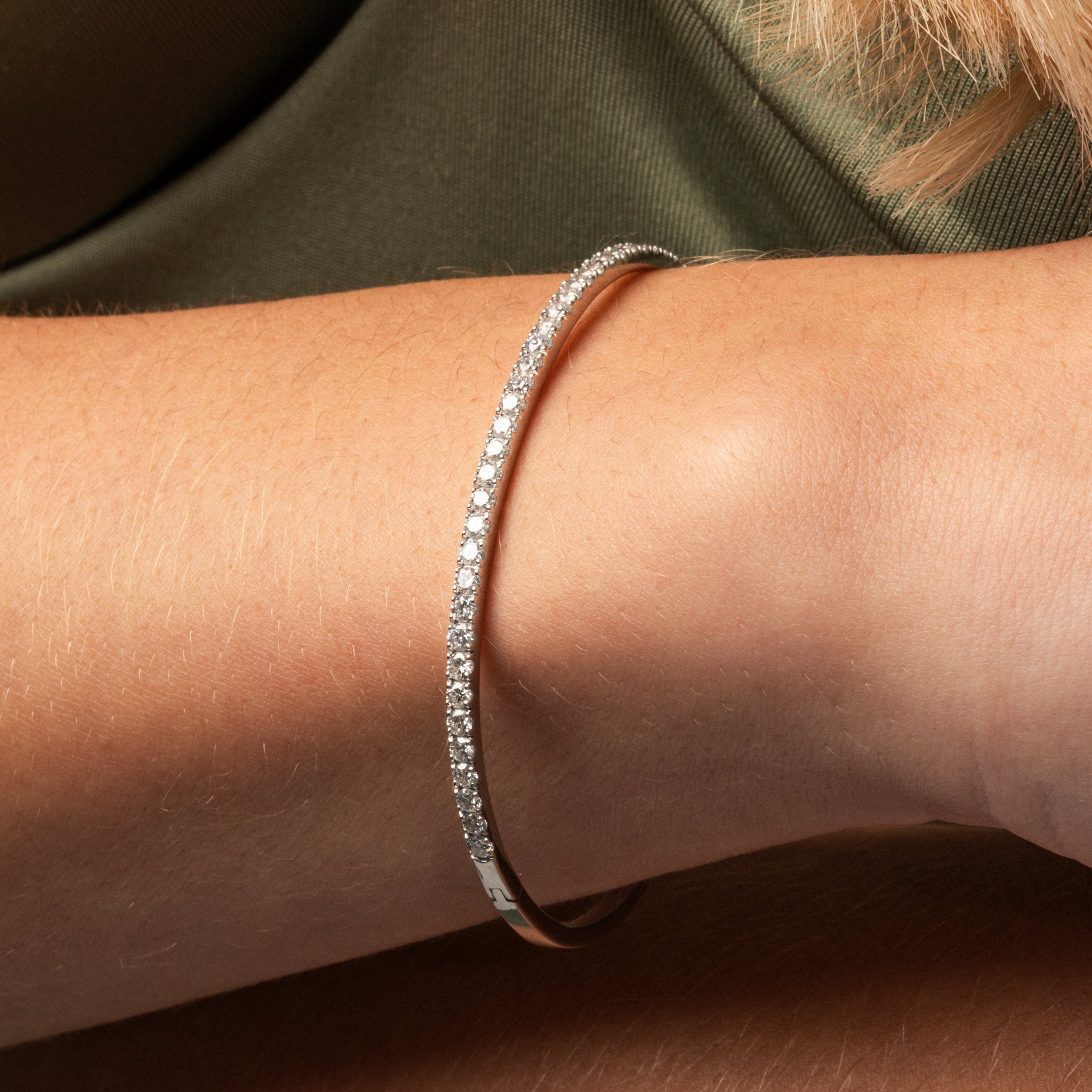 Luxury diamond tennis bangle featuring diamonds on a solid gold band worn on the wrist.