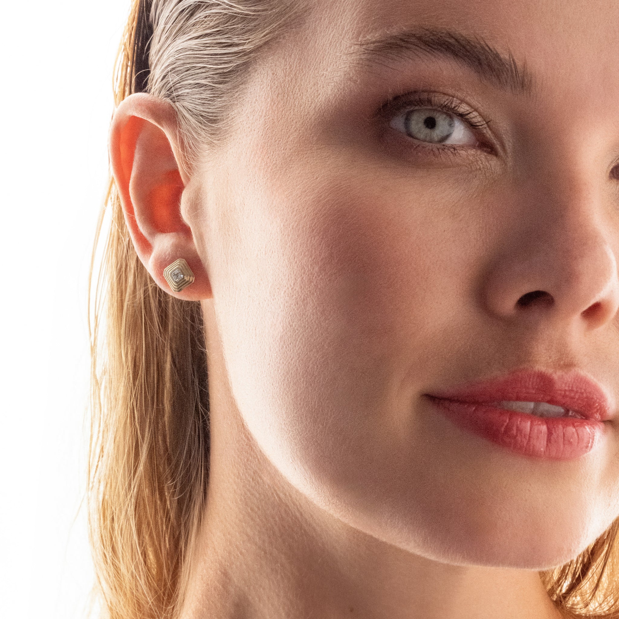 Close-up of a woman's face with a focus on her ear and asscher cut diamond earring.