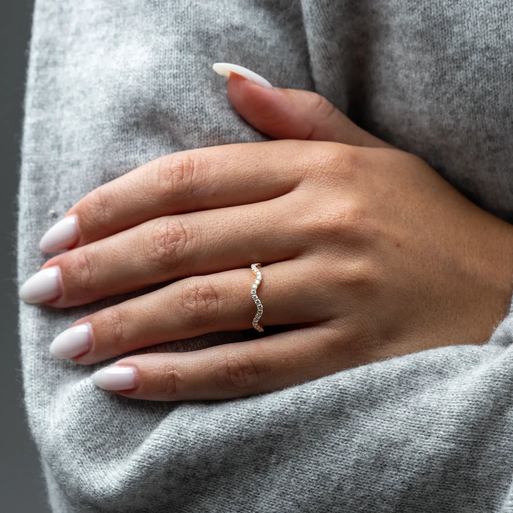 Close-up of a hand wearing a diamond ring on a gray fabric background