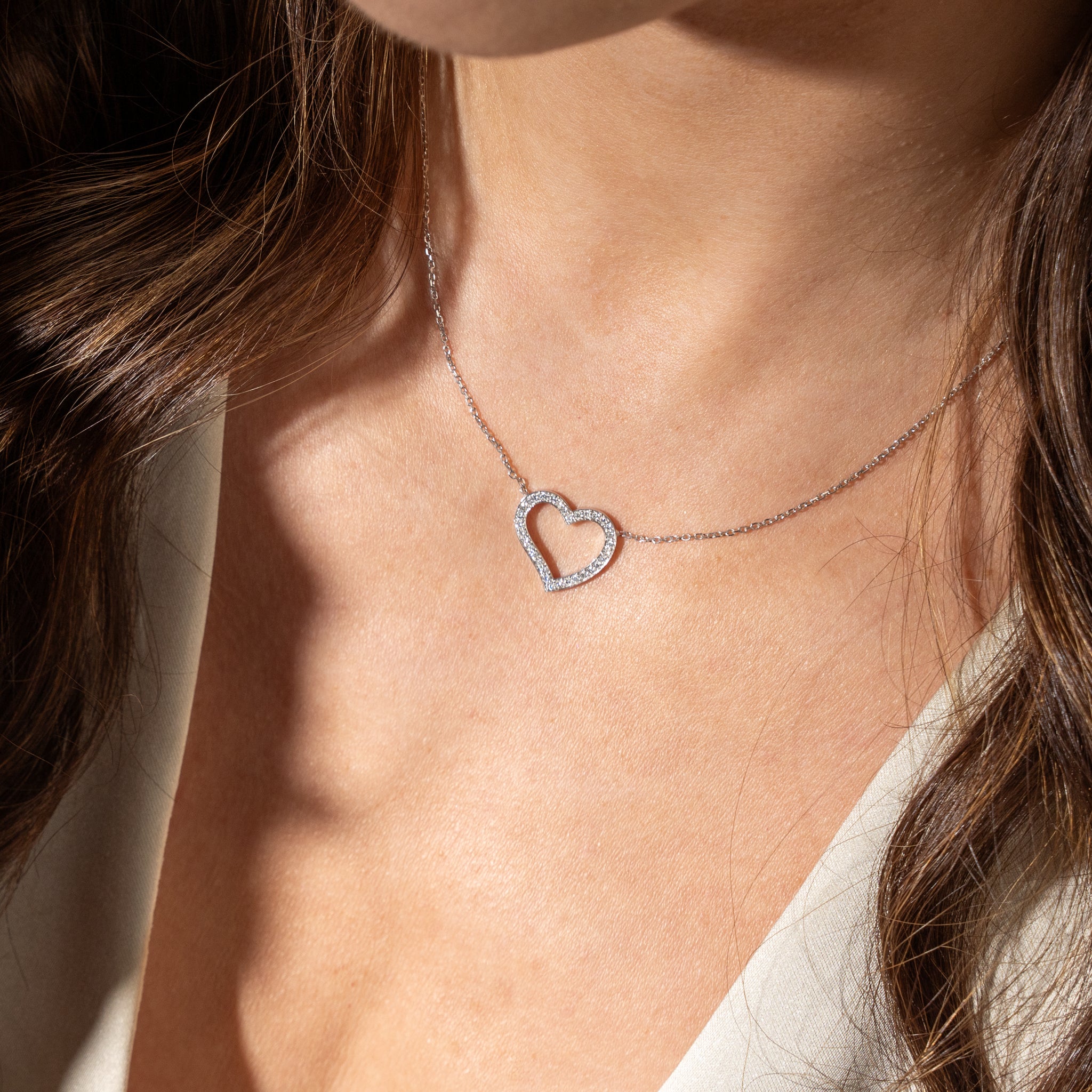 Heart-shaped diamond necklace worn by a person with sunlight casting shadows on the skin.