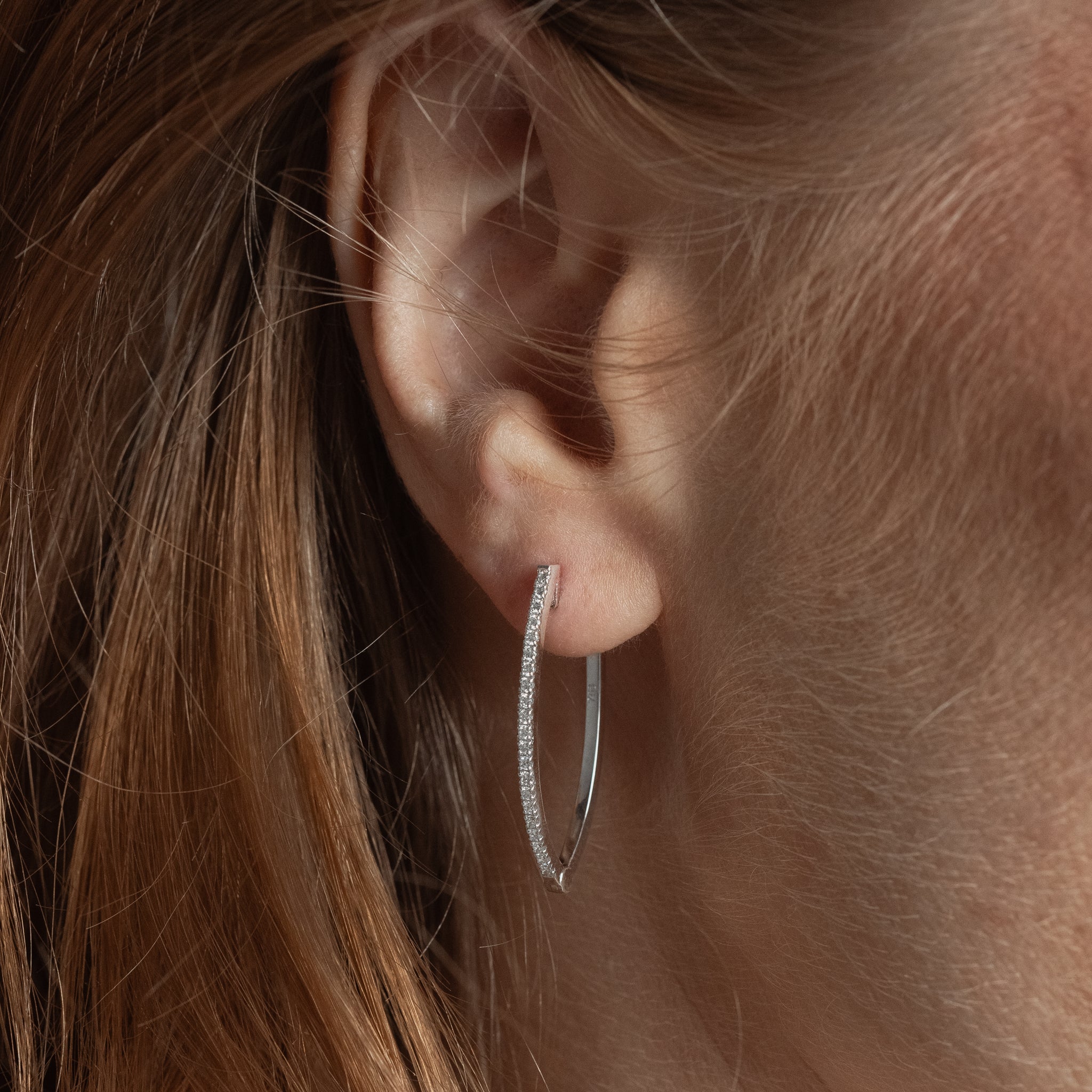 Close-up of an ear wearing a diamond hoop earring with a blurred background