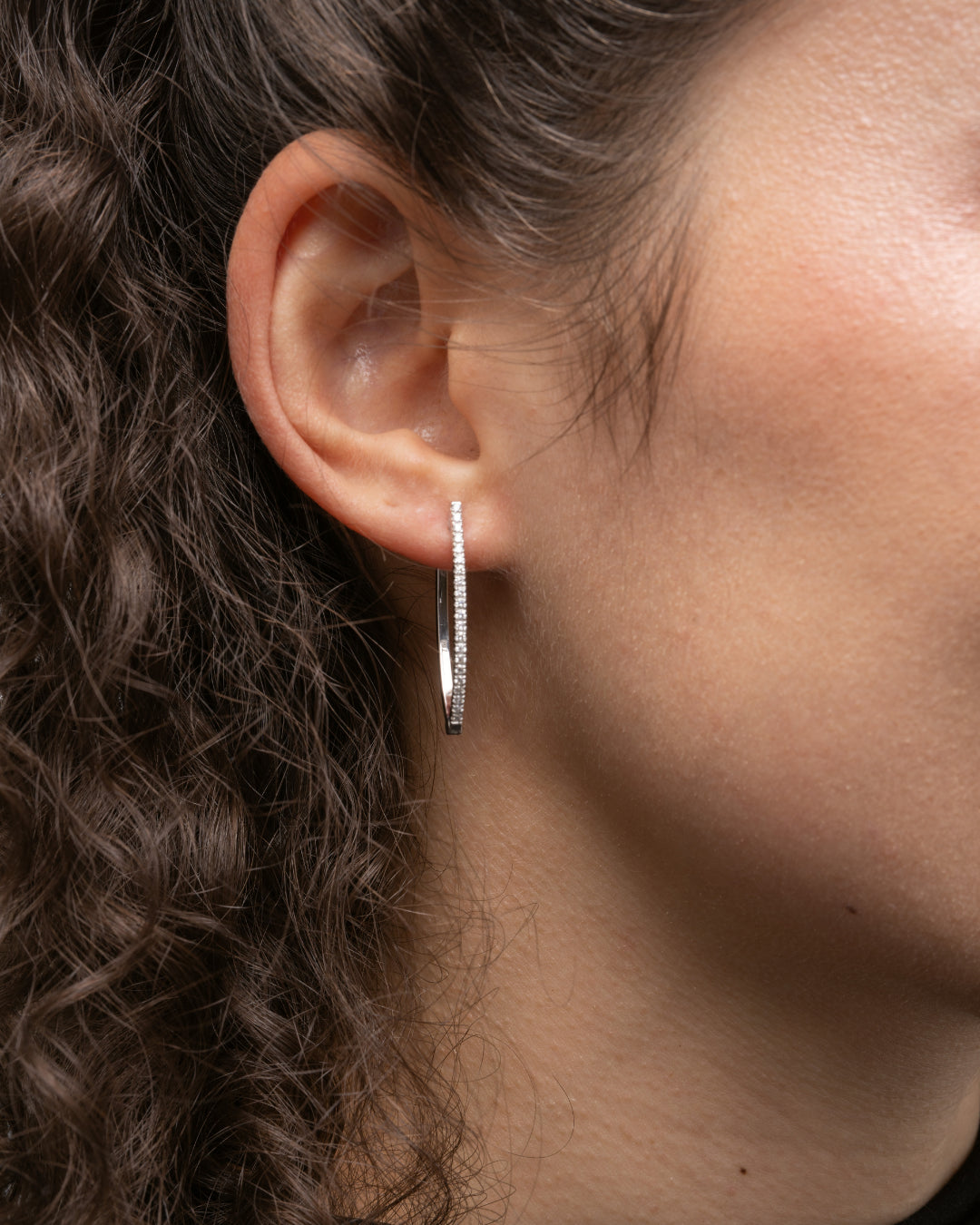 V-shaped certified diamond earrings in 18ct gold worn on a model with curly hair, showcasing modern elegance.