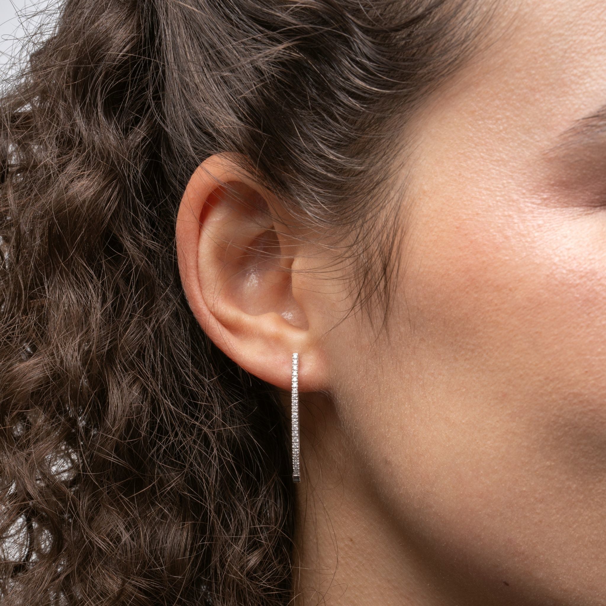 Close-up of an ear wearing a diamond hoop earring with hair partially covering the frame.
