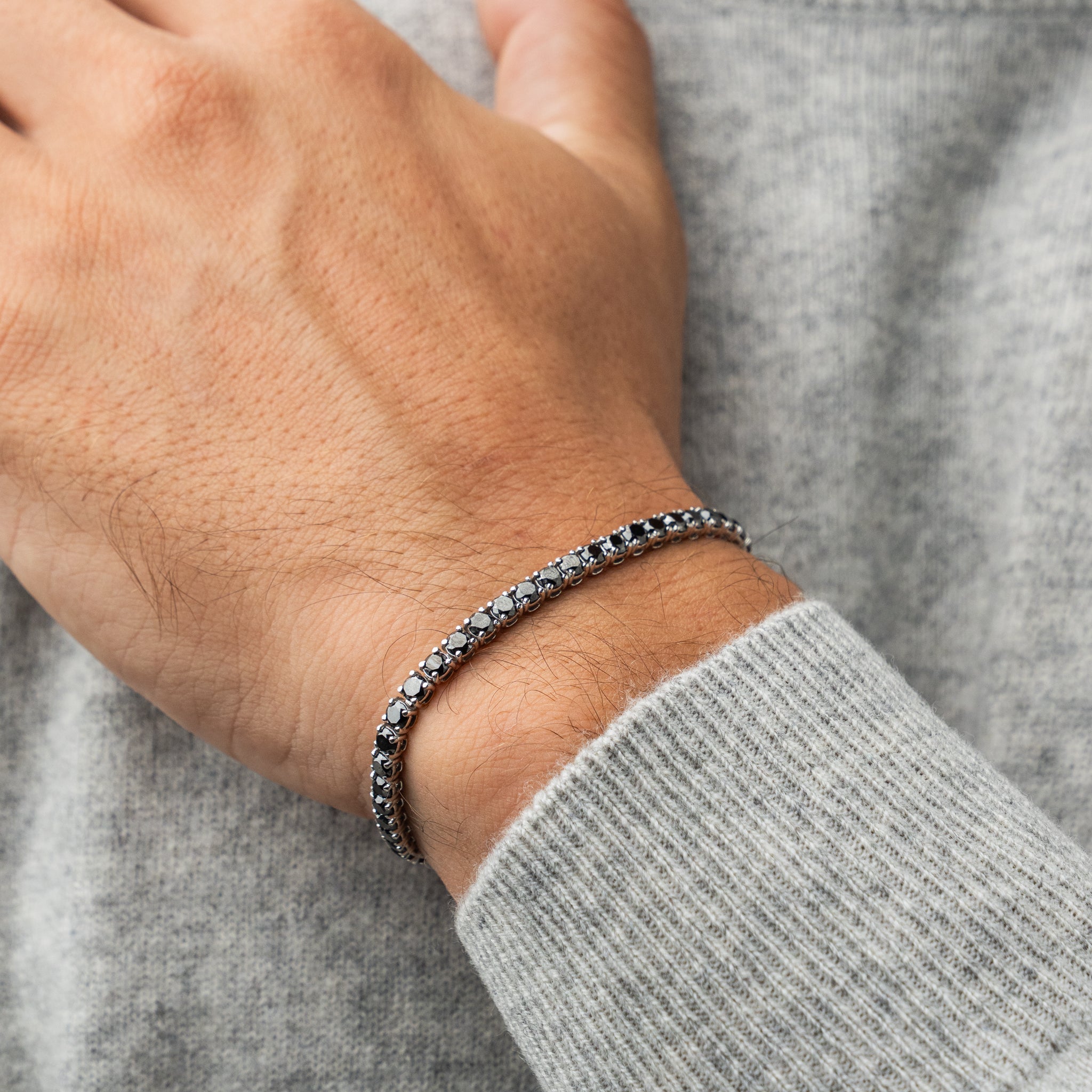 Close-up of a hand wearing a black diamond tennis bracelet with a gray sweater sleeve.
