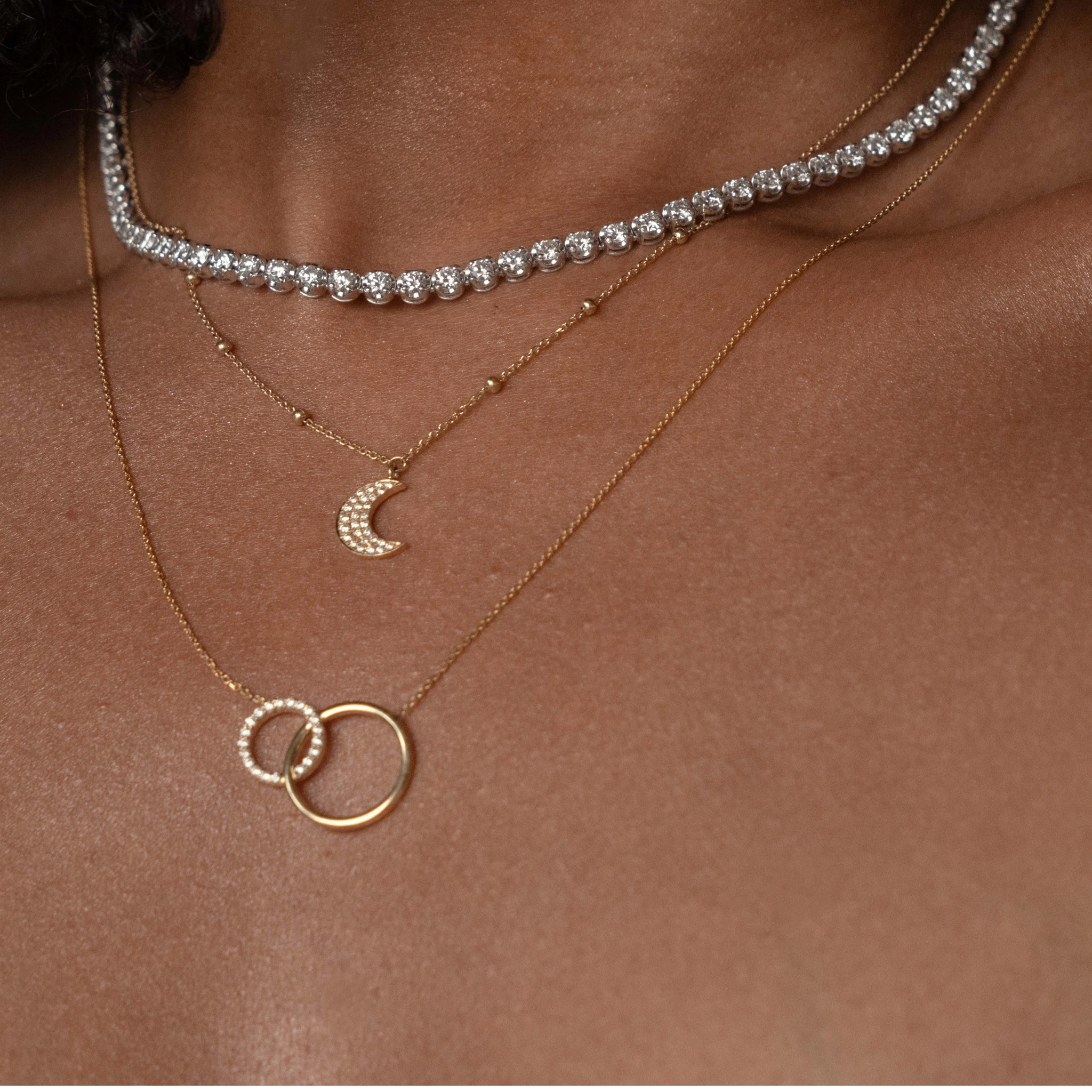 Close-up of layered gold necklaces featuring a diamond necklace with a half moon pendant.