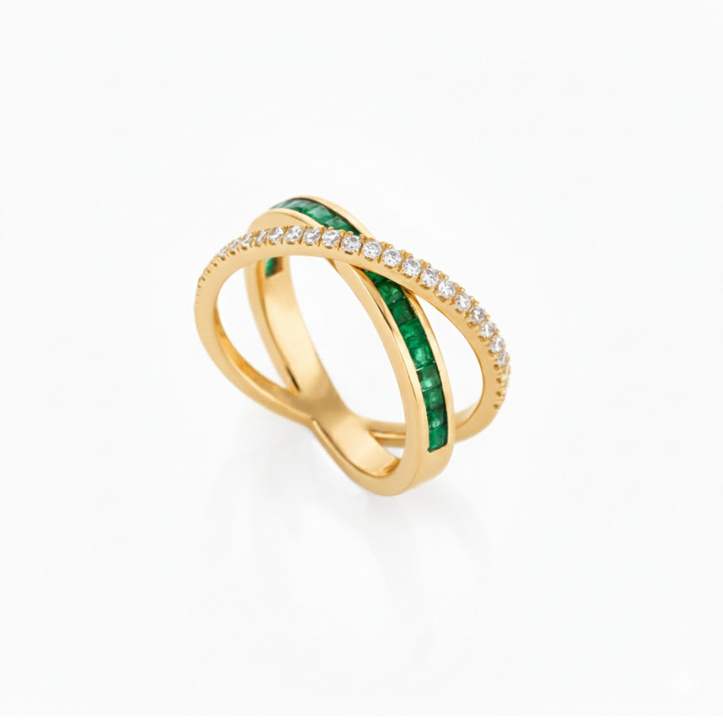 Gold criss cross ring with emeralds and diamond accents on a white background