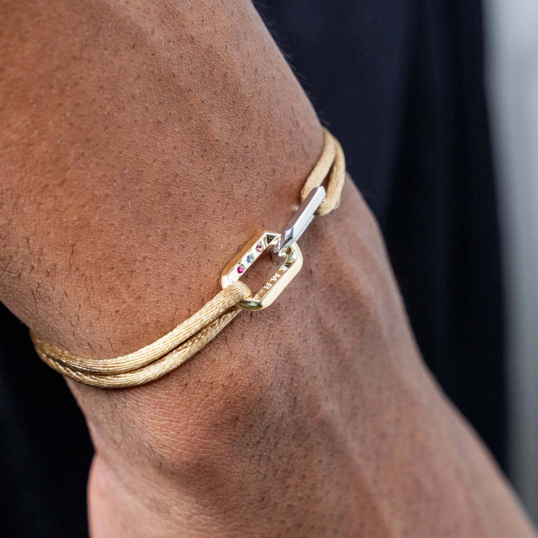 Close-up of a wrist wearing a brown leather bracelet with gold chains