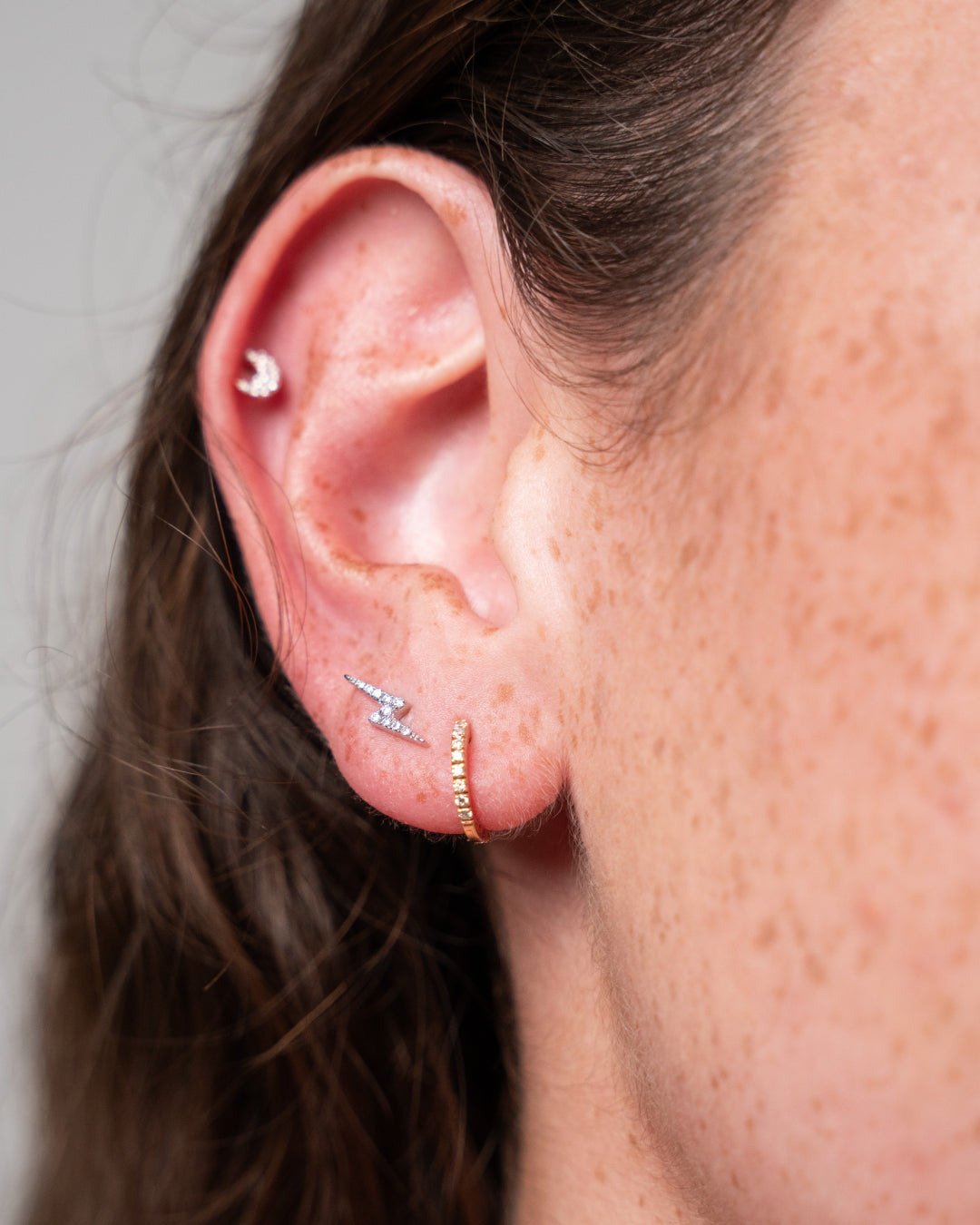 Close-up of ear showcasing lightning bolt earrings set with certified diamonds, highlighting elegance and sparkle.
