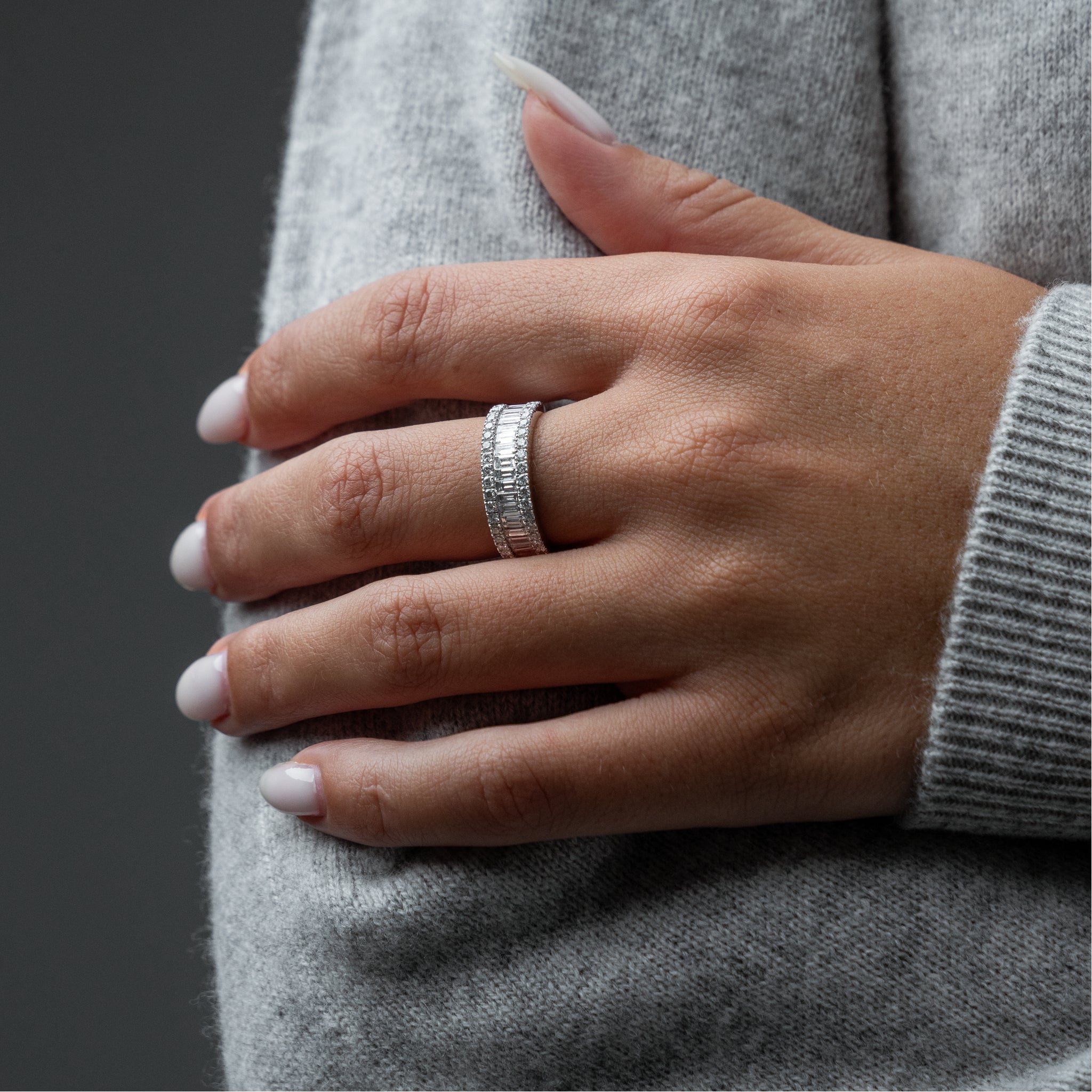 Hand wearing a white gold ring on a gray background