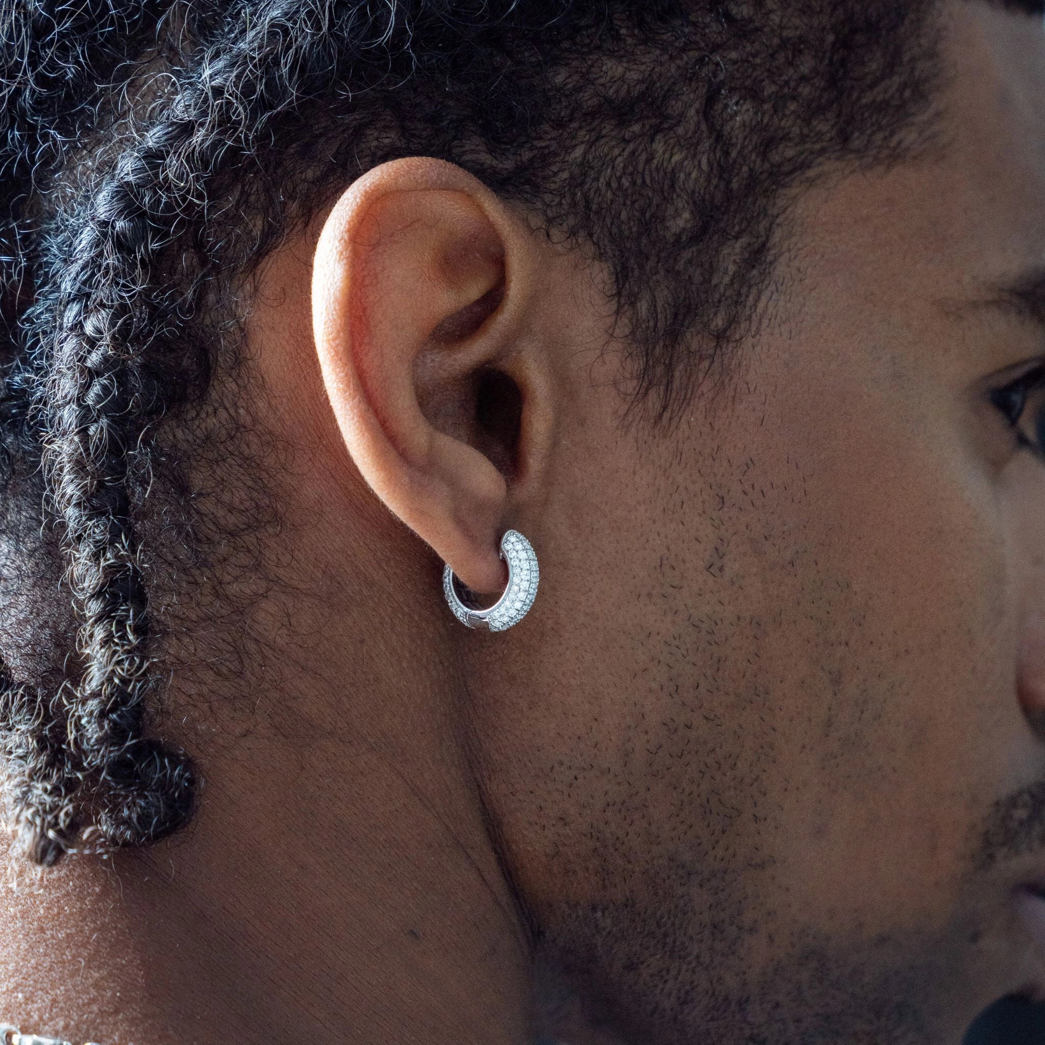 Close-up of a person wearing diamond huggies earrings, showcasing the pavé diamonds set in white gold.