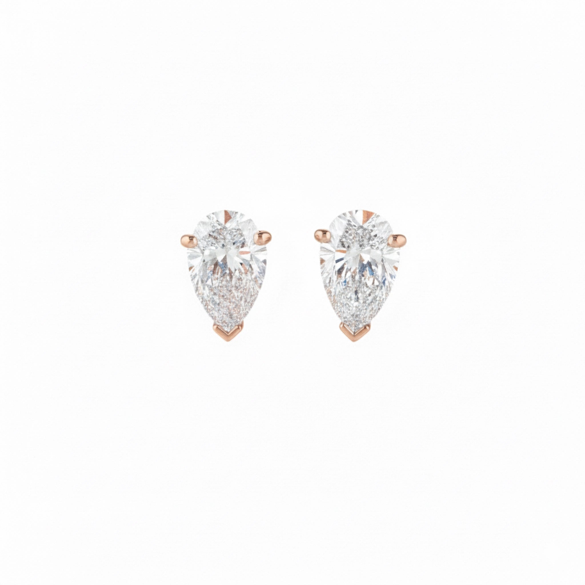 Pair of pear-shaped diamond earrings with rose gold settings on a white background