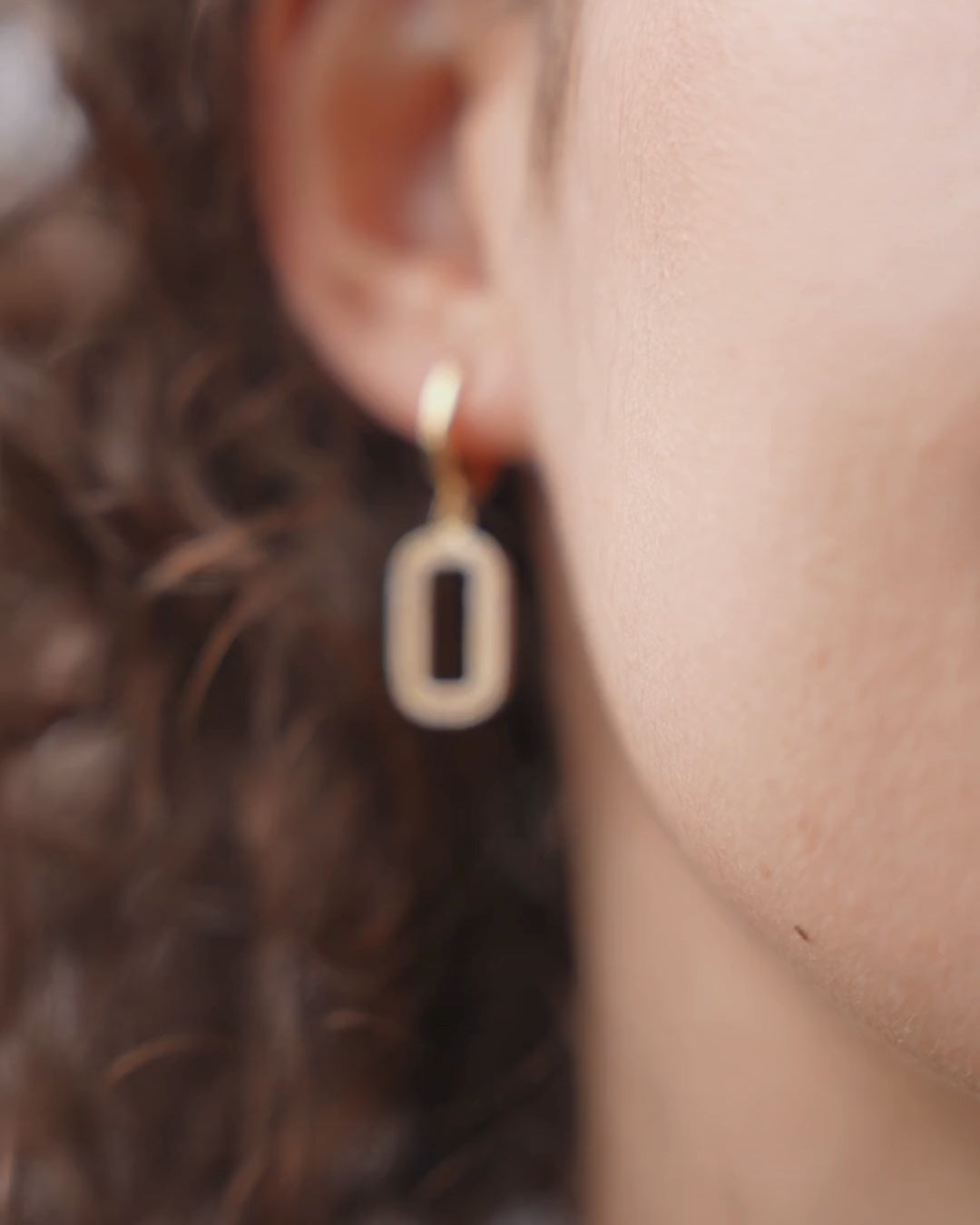 Elegant gold Niamh earrings featuring diamond drop design worn on a model with curly hair.