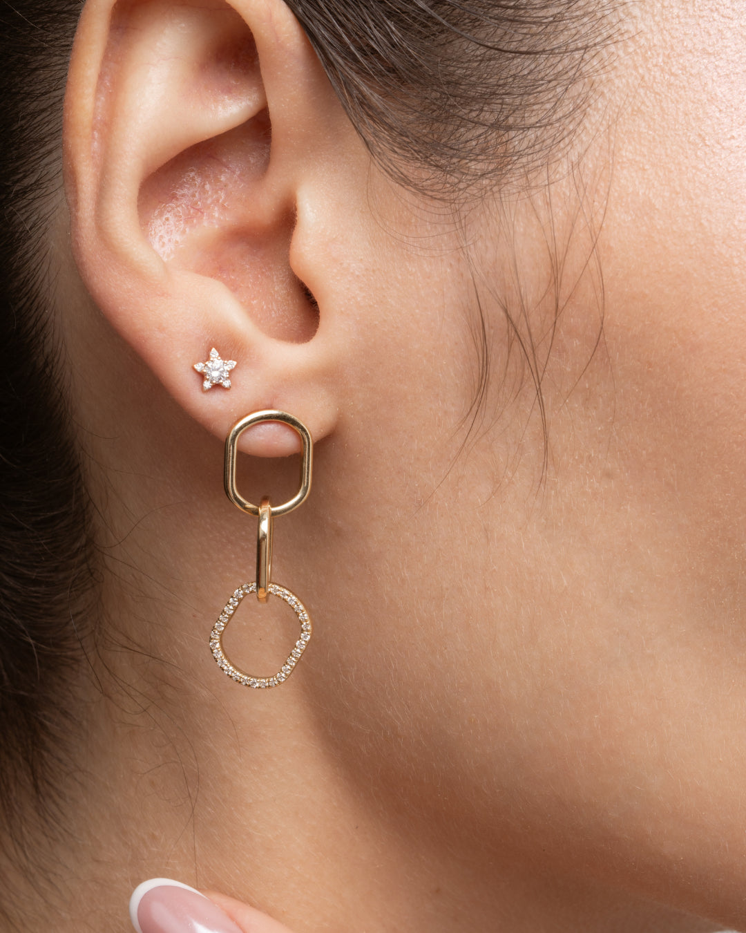 Close up of a woman's ear showcasing chain link diamond earrings and a solid gold star earring, highlighting style and elegance.