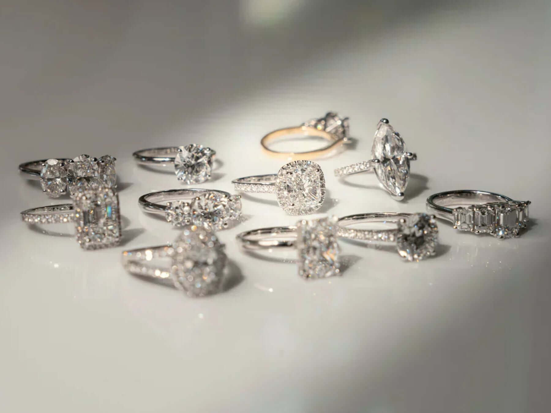 Various diamond jewellery engagement rings displayed elegantly on a reflective surface.