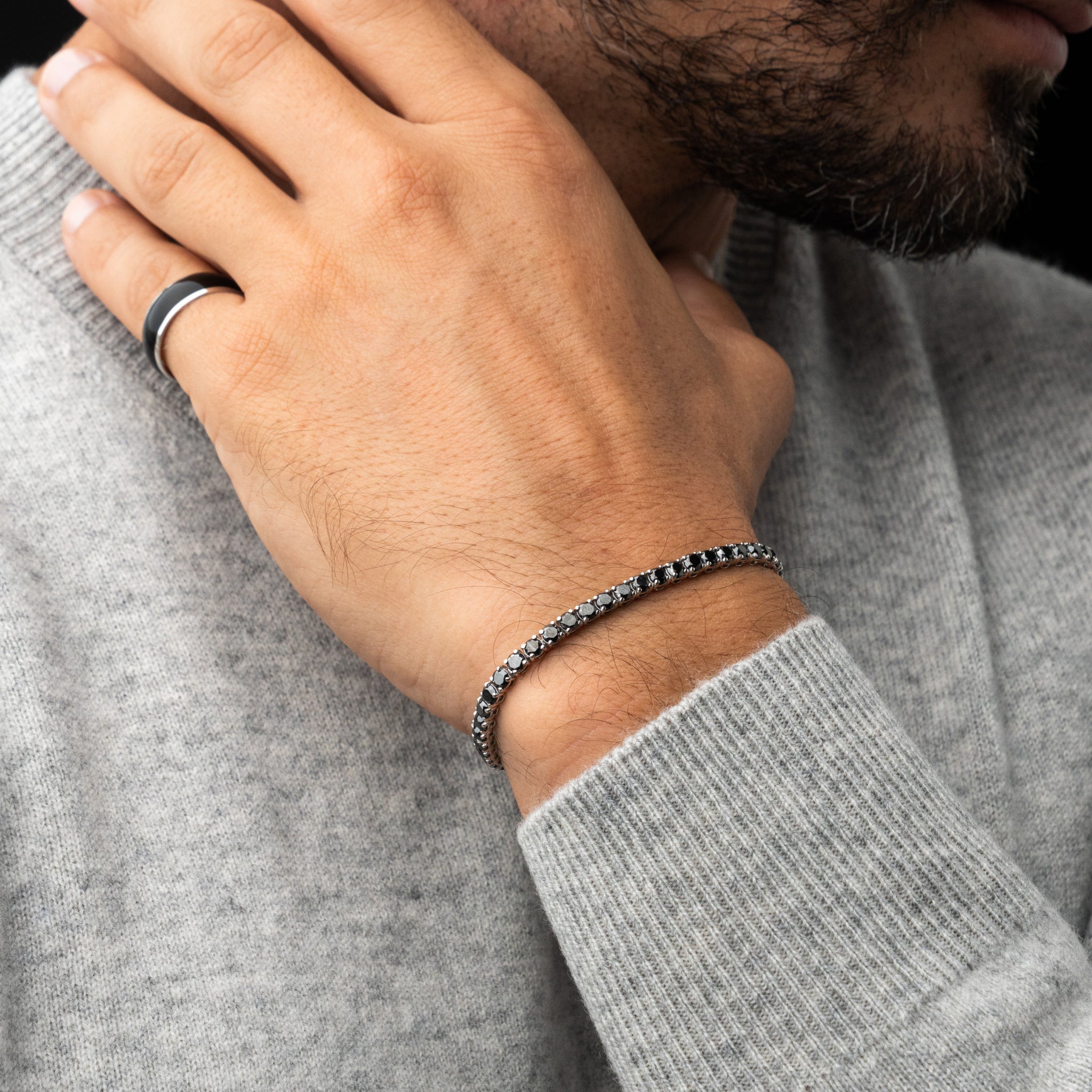 Person wearing a black diamond tennis bracelet and wearing a grey sweater