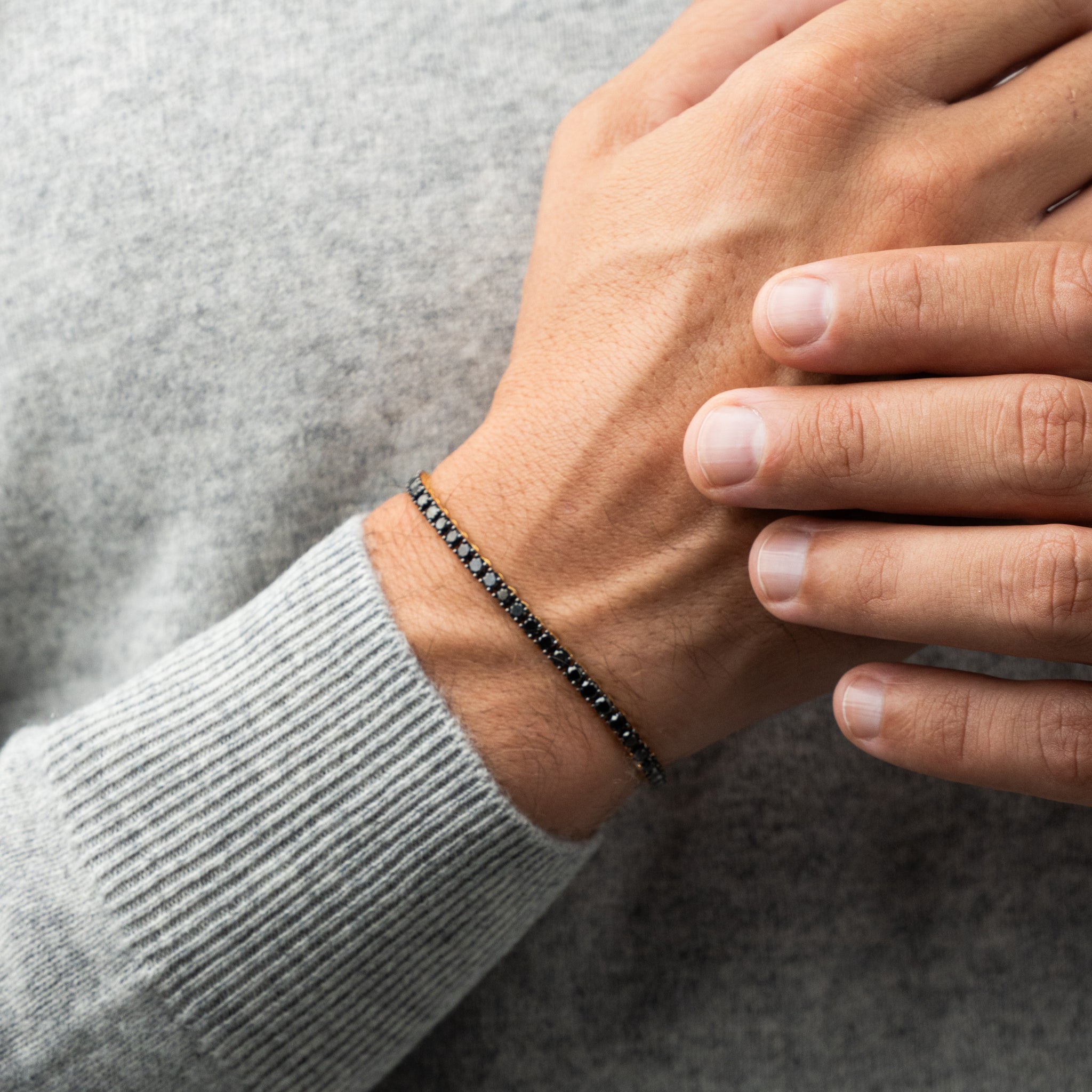 Person wearing a black diamond tennis bracelet on a grey sweater background