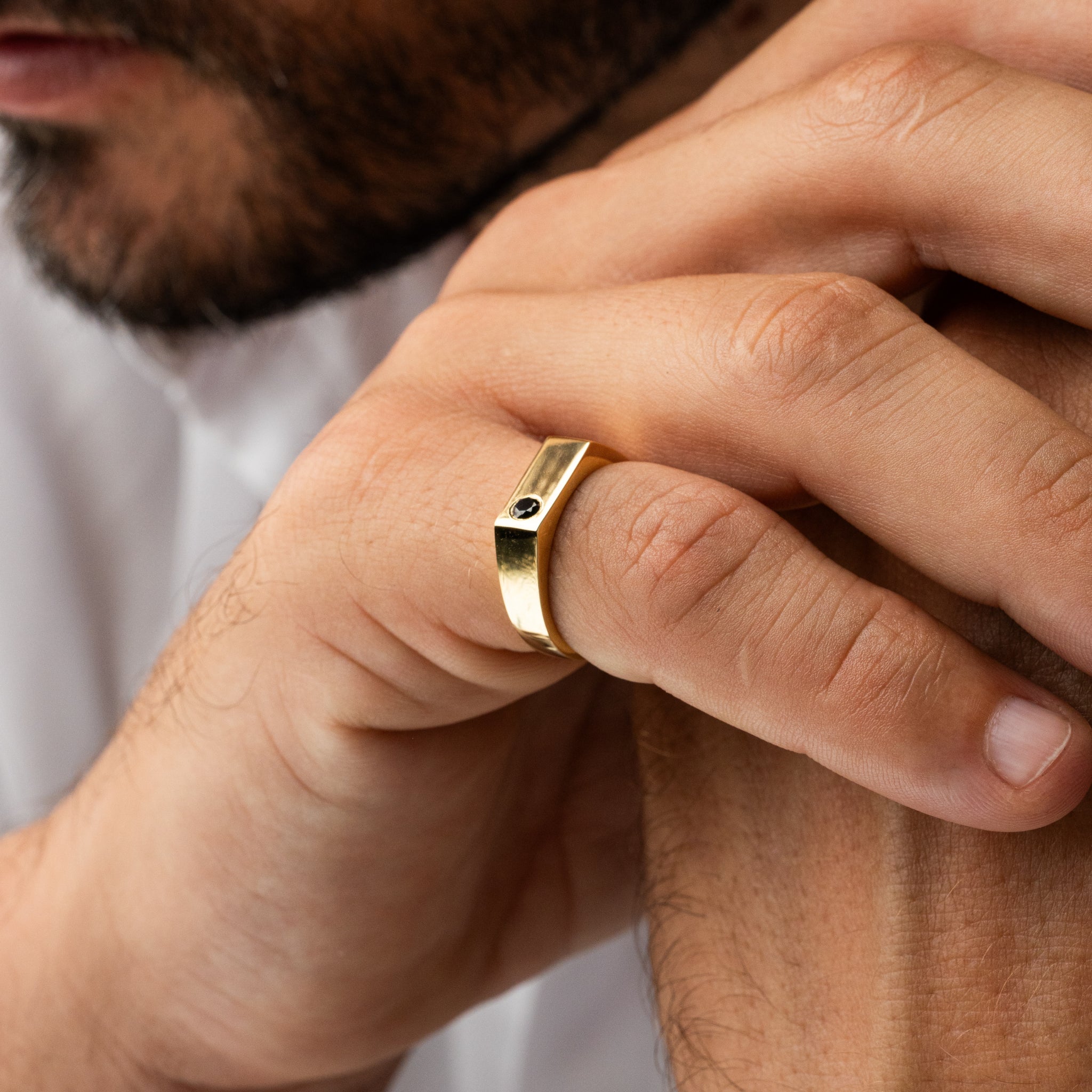 Close-up of a hand wearing a gold ring with a black stone.