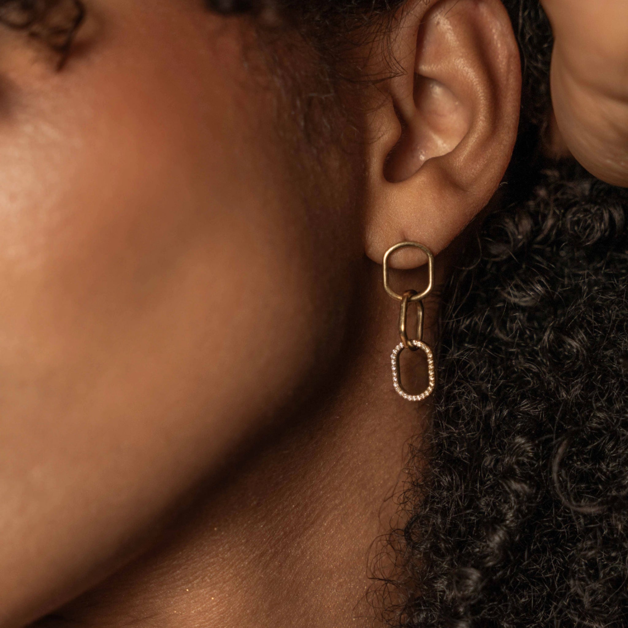 Close-up of model wearing chain link diamond earrings showcasing interlocking links in 18ct gold with certified diamond accent.