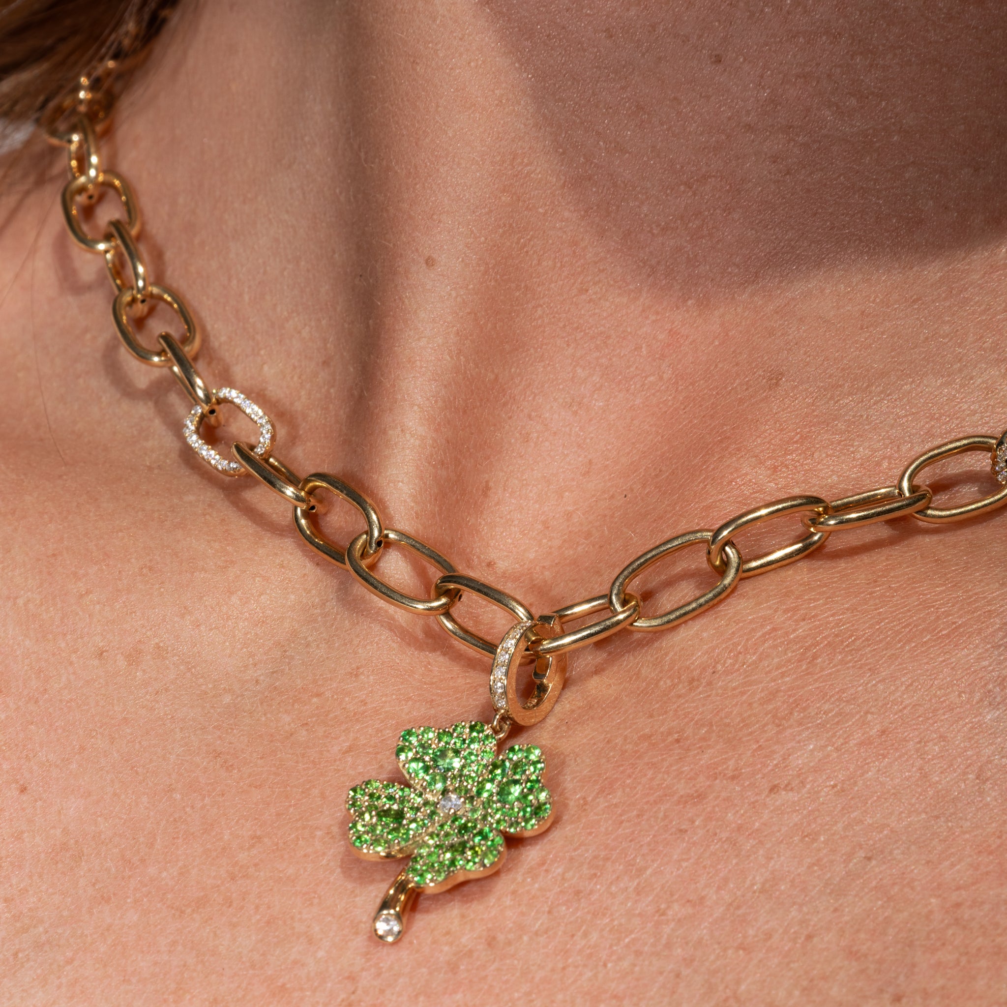 Gold chain necklace with a tsavorite green clover pendant on a person's neck.