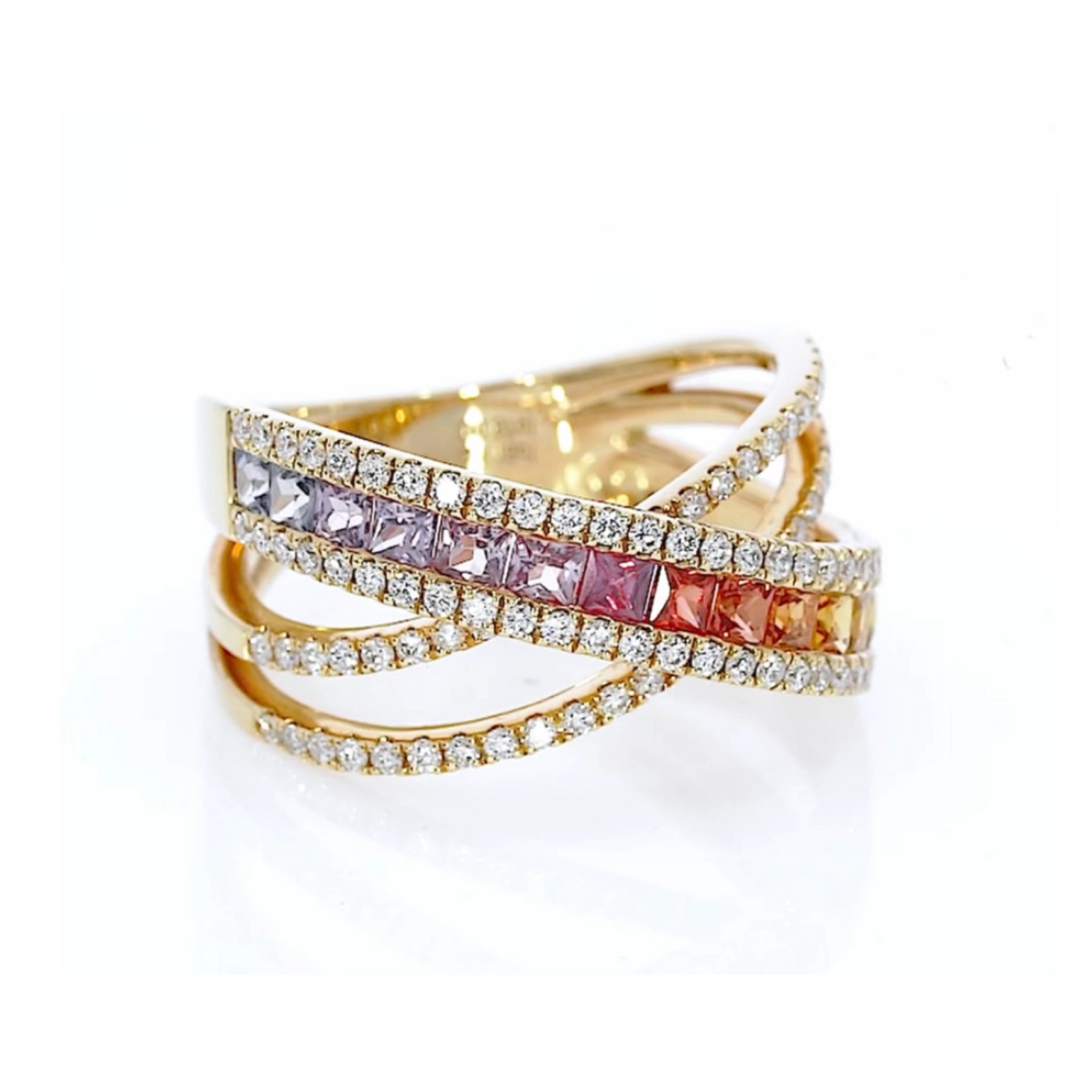 Criss cross ring featuring fifteen coloured sapphires in green to blue hues, and round brilliant diamonds, set in 18ct gold.