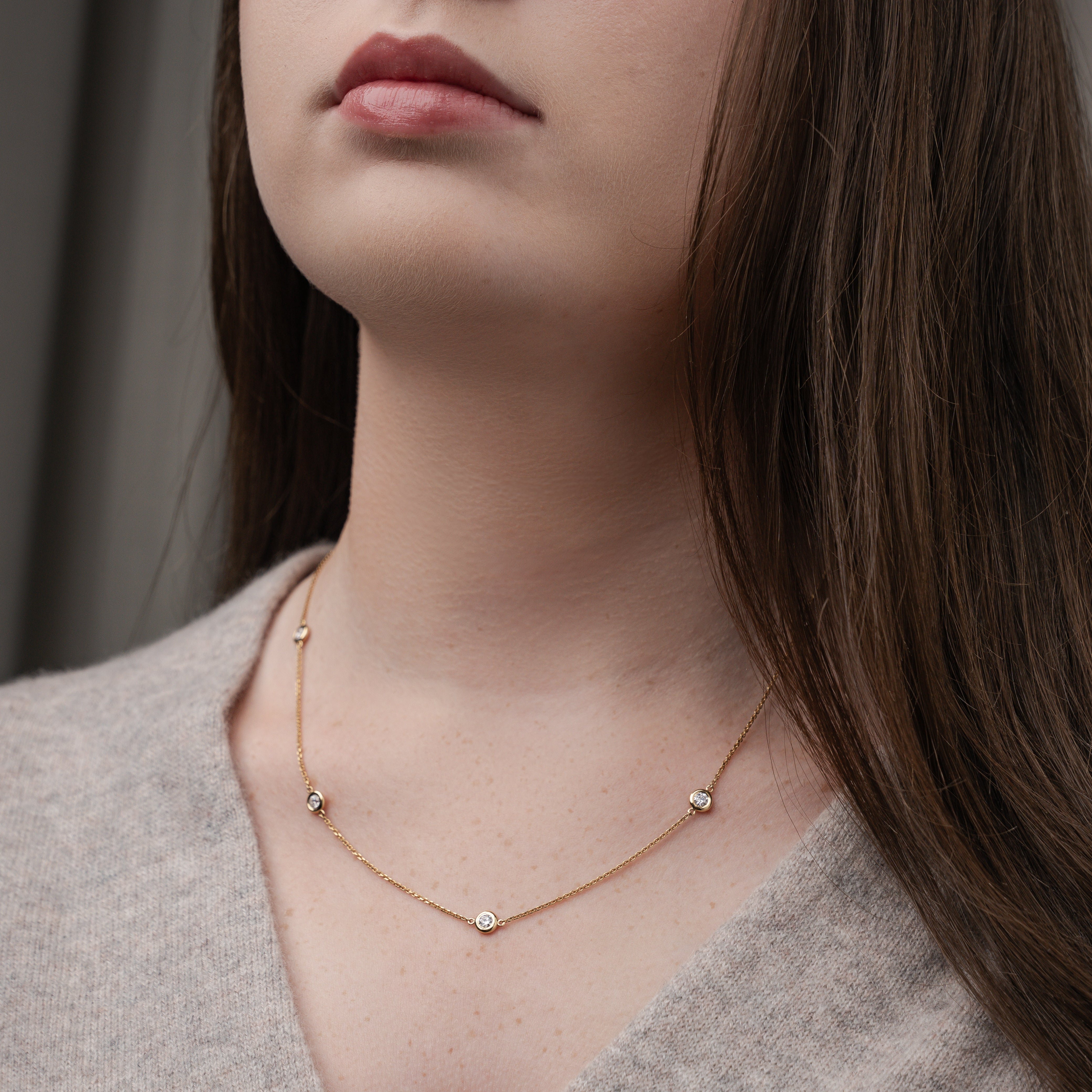 Close-up of a woman wearing a certified diamond necklace on a delicate chain with a beige top.