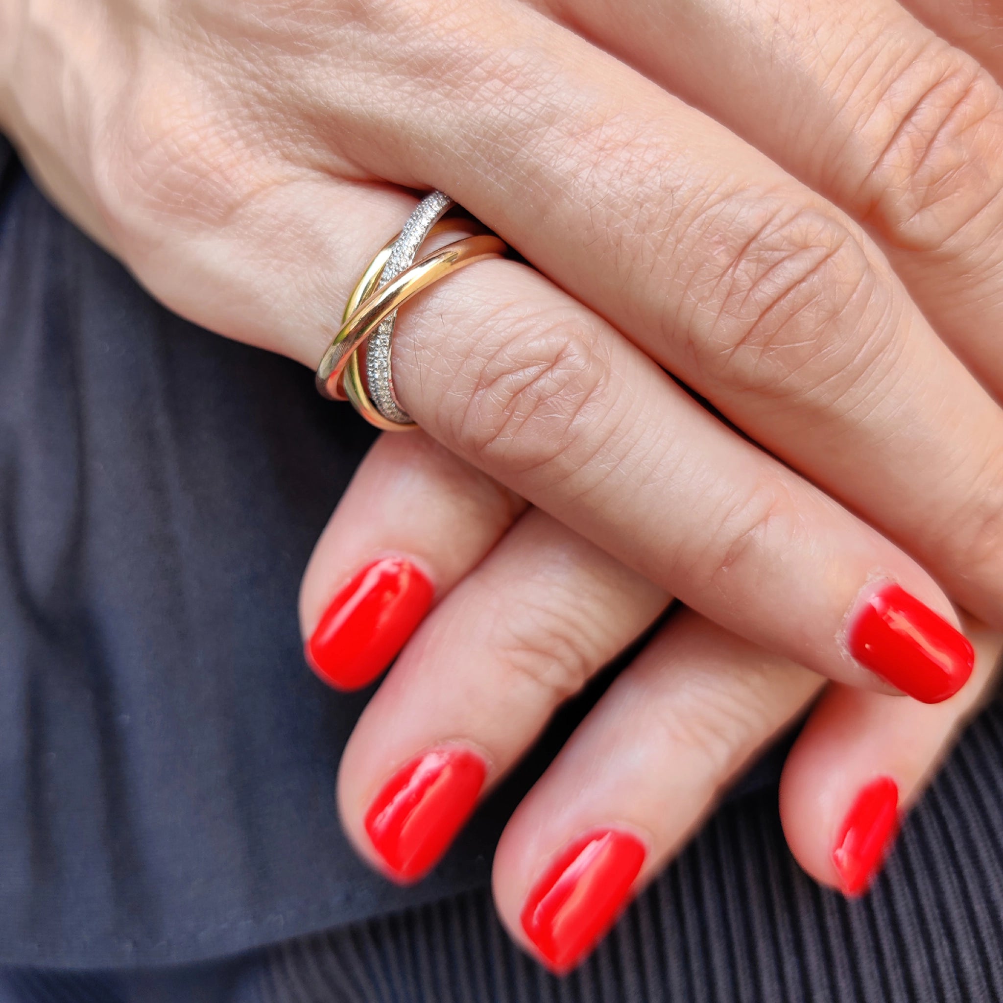 Grace Ring featuring three intertwined solid gold bands and diamonds, elegantly displayed on a hand with red nails.