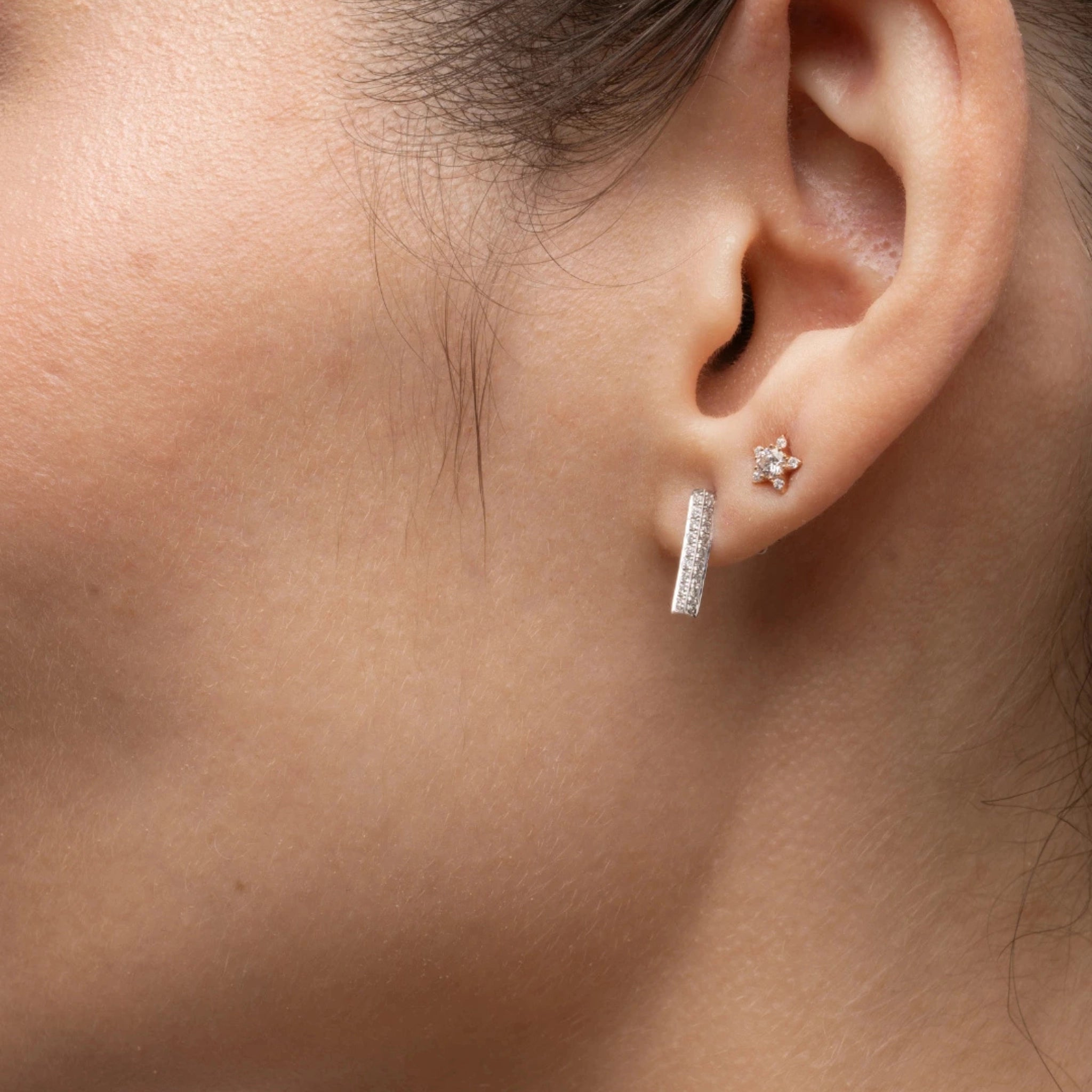 Model showcasing certified diamond earrings in gold bar style alongside a floral stud earring.