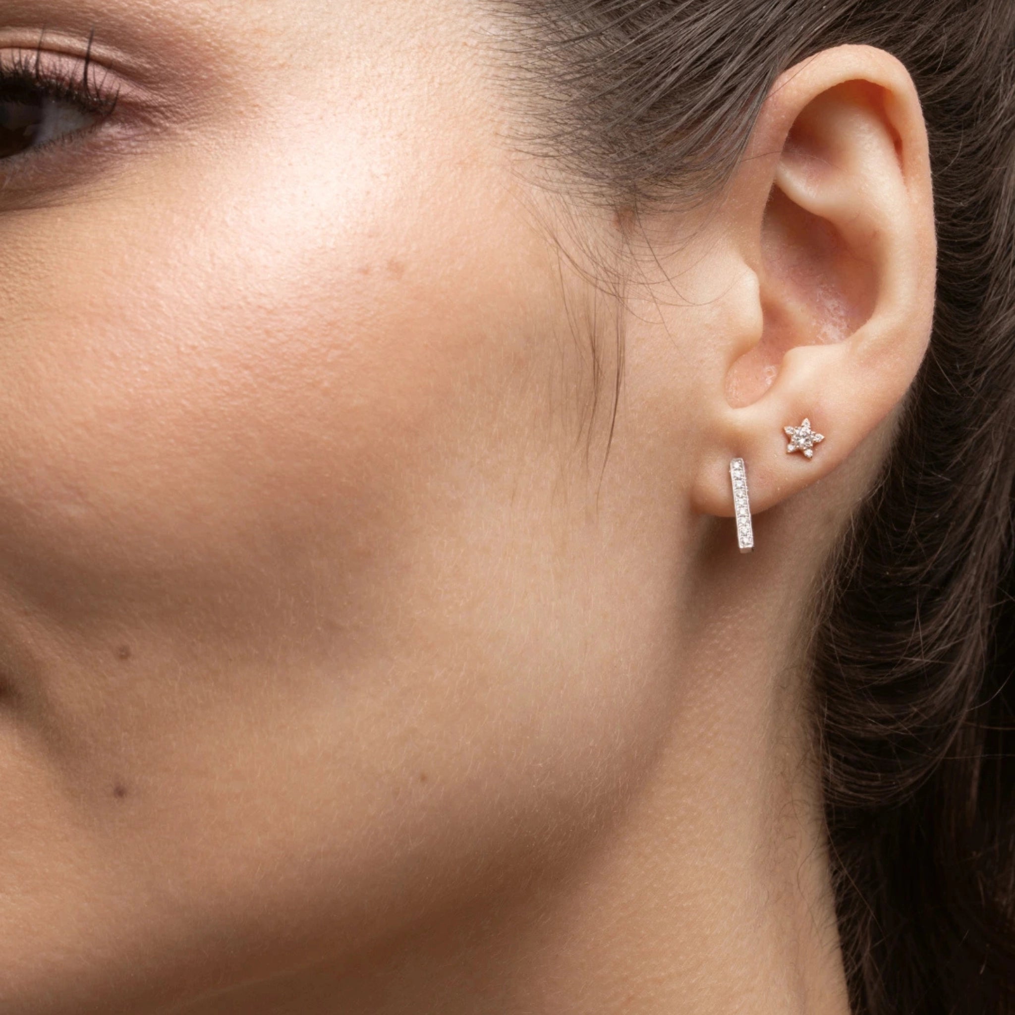 Close-up of a woman's ear featuring certified diamond earrings, showcasing a star design with sparkling diamonds.