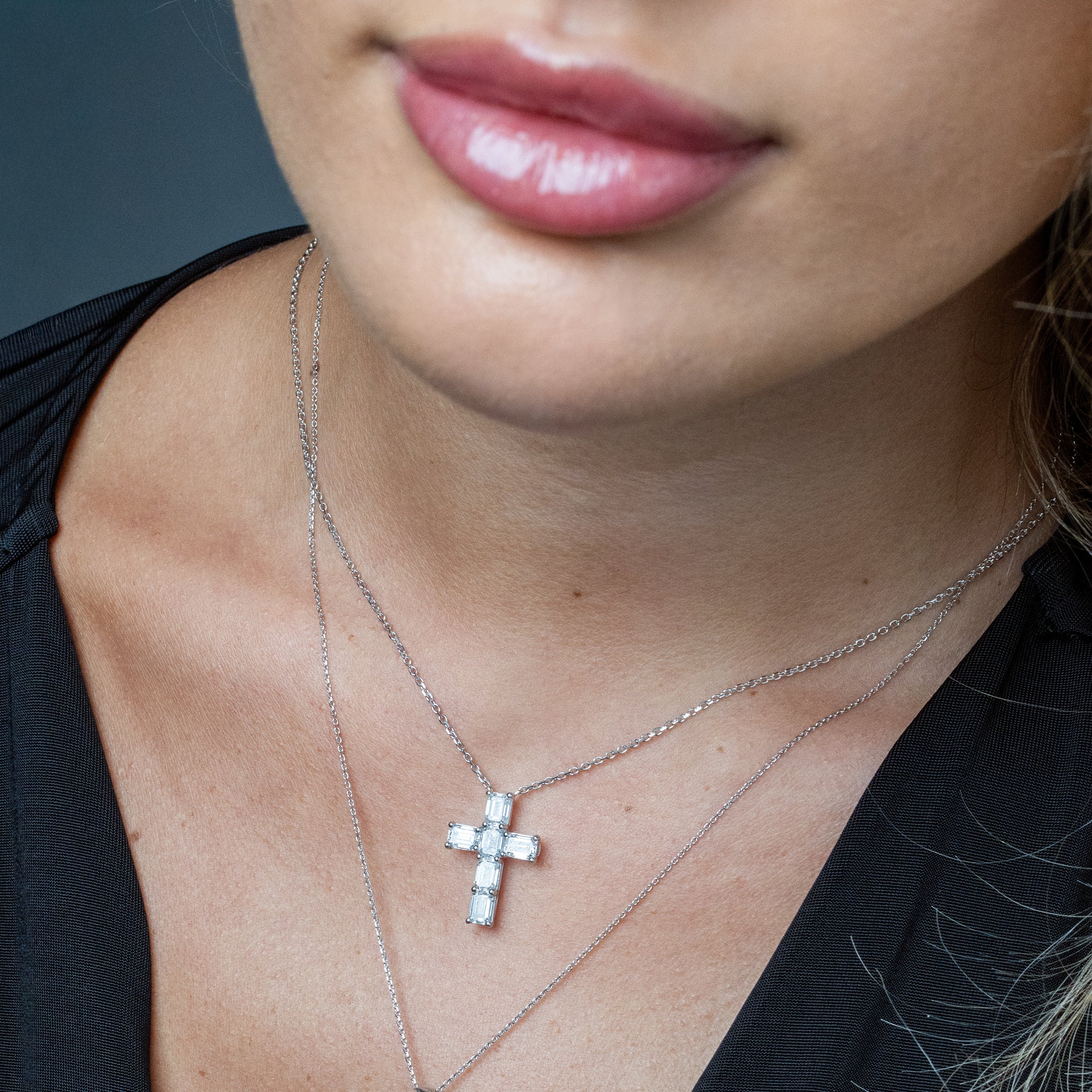 Close-up of a person wearing a diamond cross necklace with a blurred background