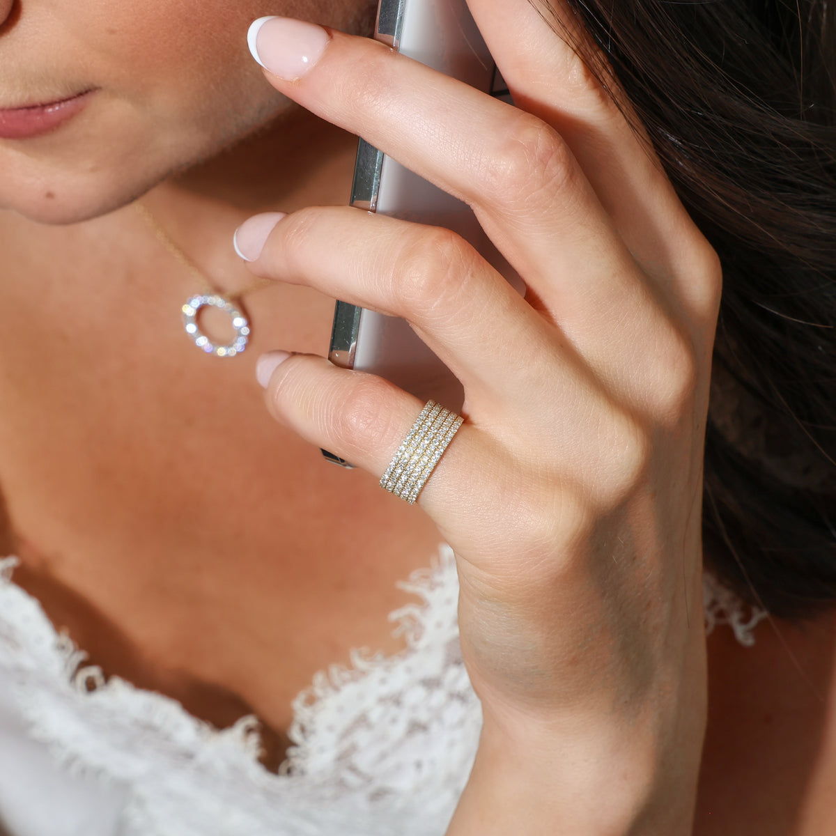 A close-up lifestyle shot of a woman wearing a multi-row diamond ring on her finger, holding a smartphone to her ear.  