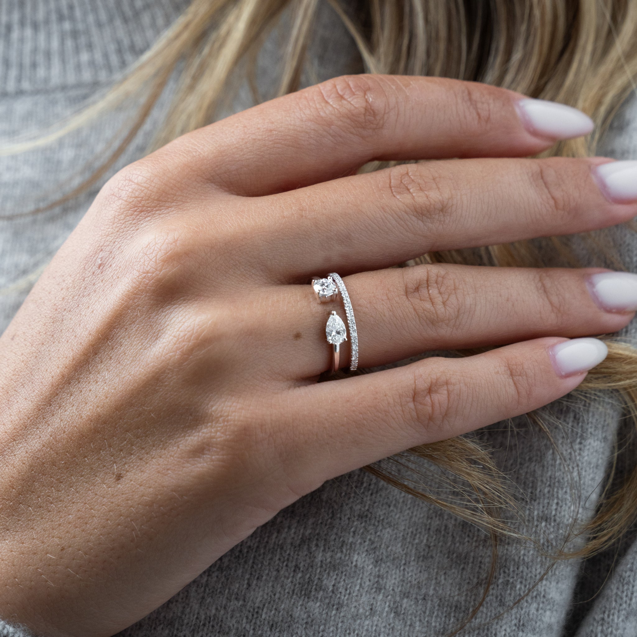 Close-up of a hand wearing a white gold ring with diamonds on a neutral background
