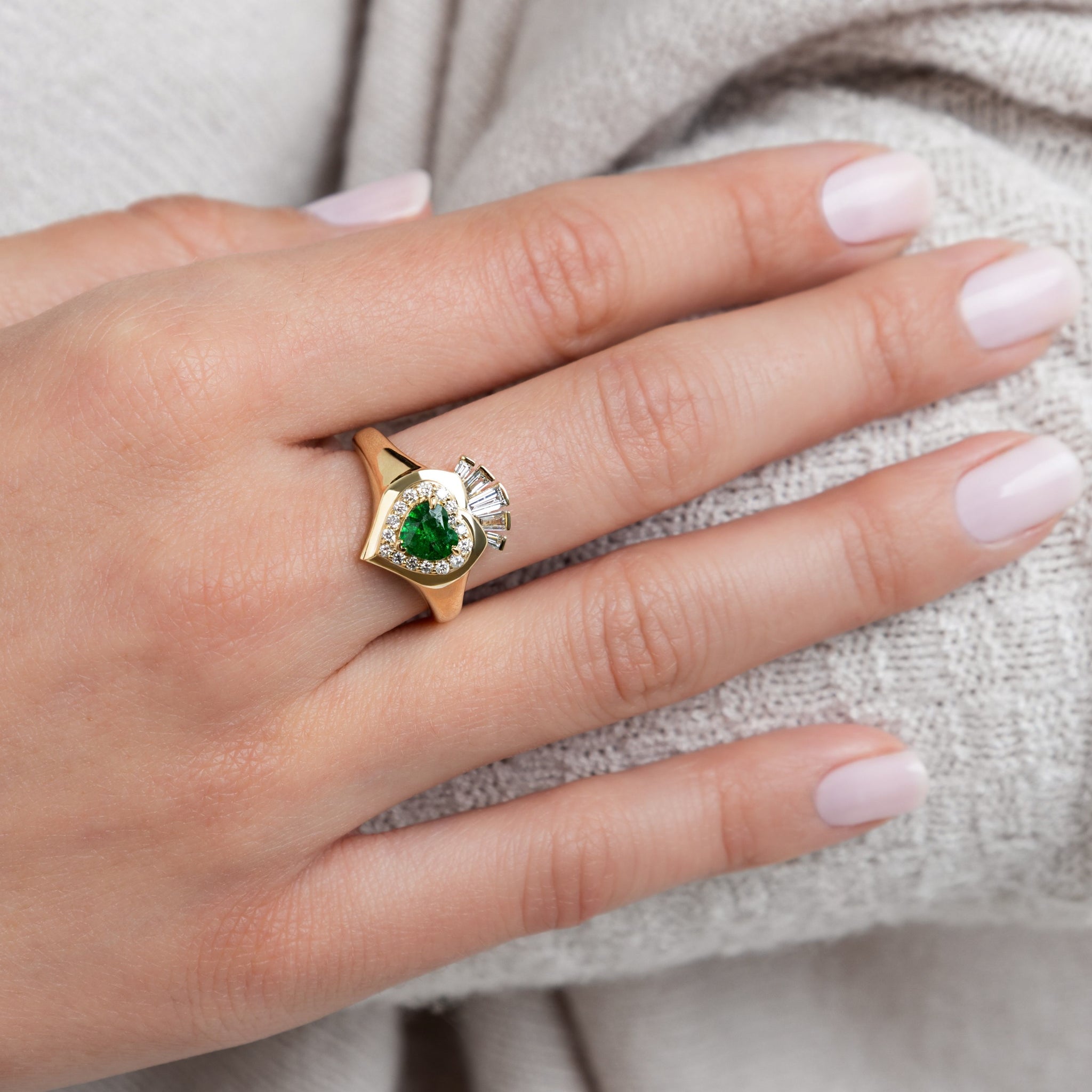 Éireann Claddagh ring displayed on a hand, featuring a green tsavourite and intricate design, symbolizing Ireland's heritage.