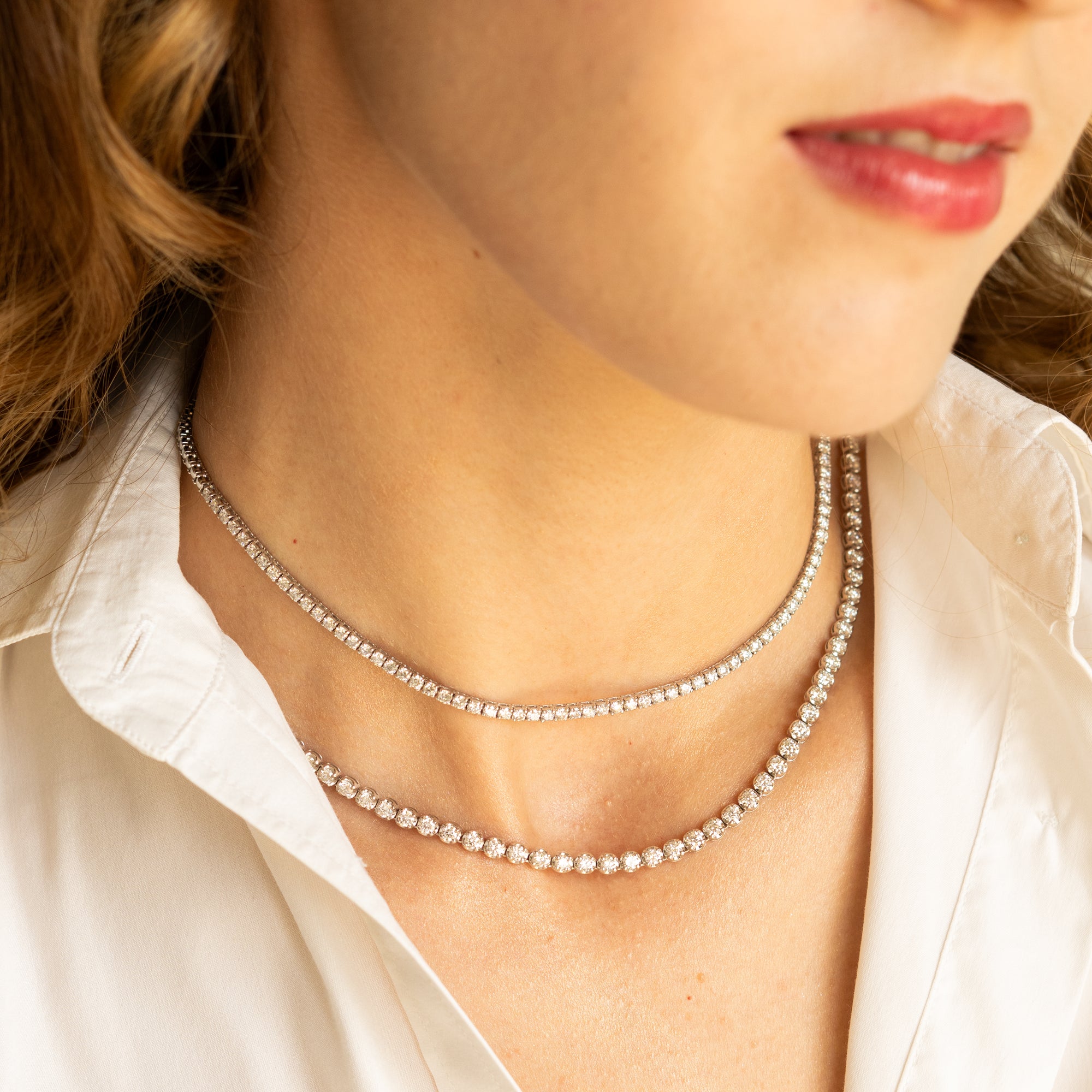 Close-up of a woman wearing a diamond tennis necklace with a white shirt.