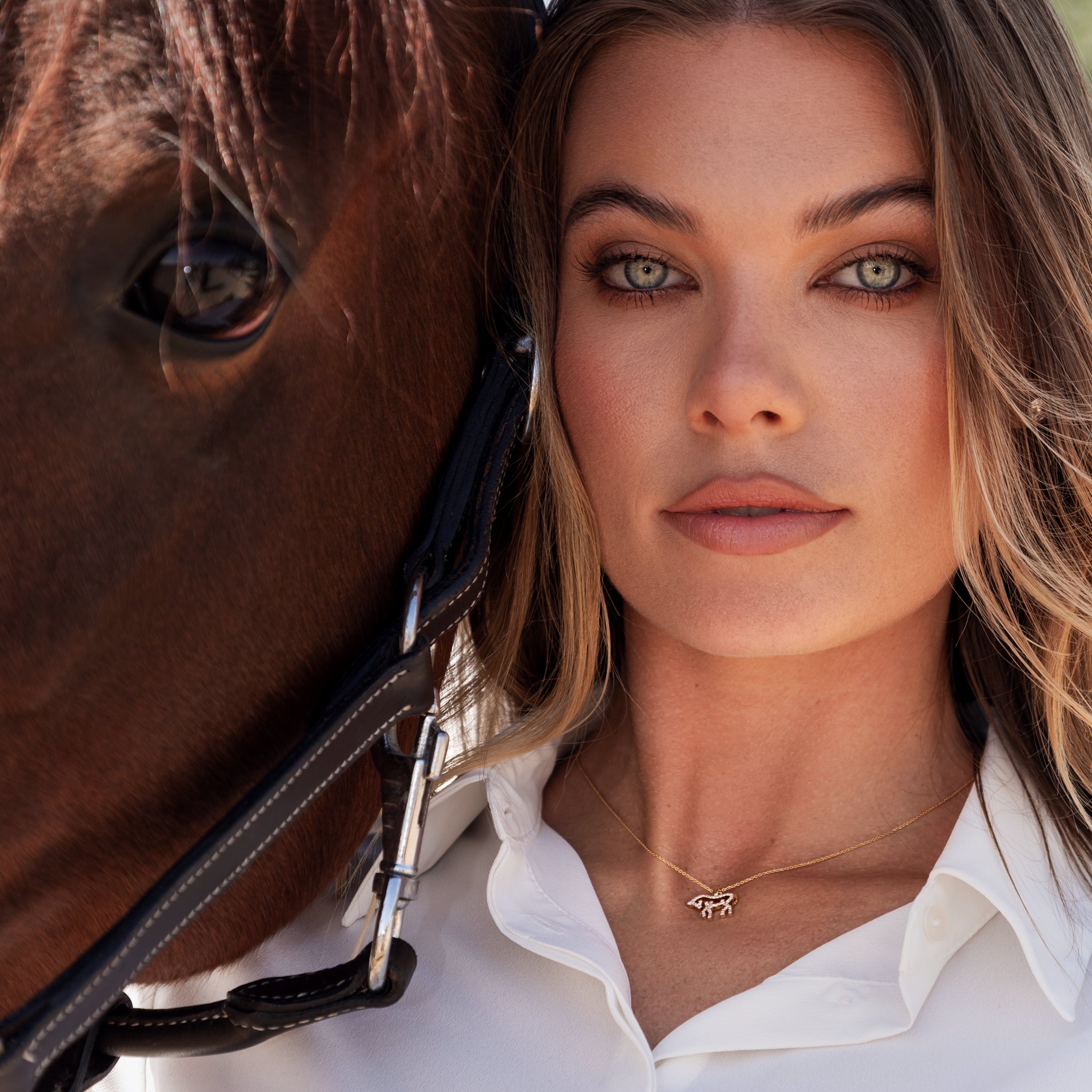 Woman wearing a diamond horse necklace next to a horse.