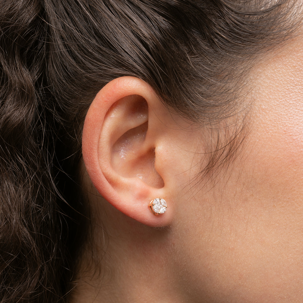 Close-up of an ear wearing a diamond earring with a neutral background