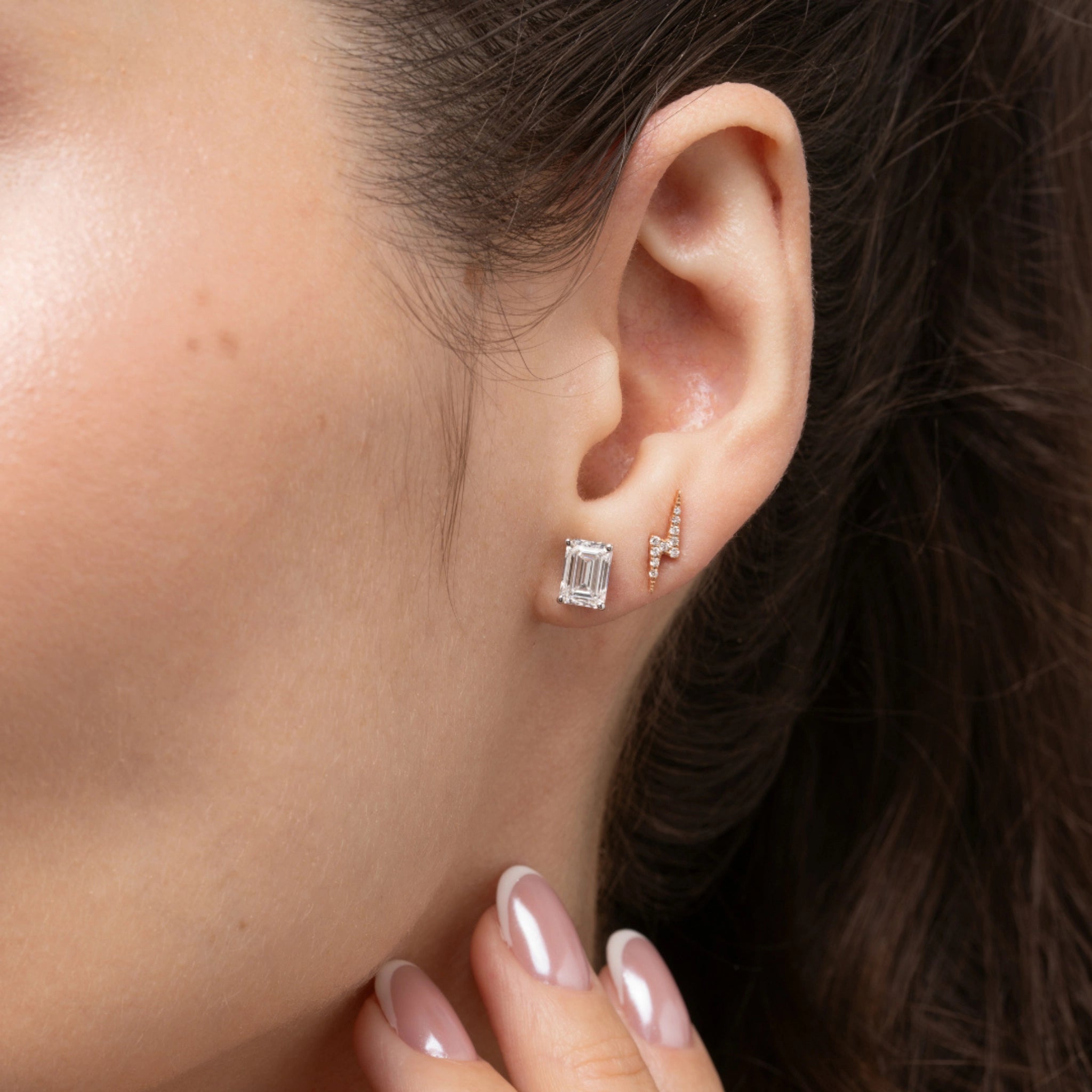 Model showcasing lightning bolt earrings in solid gold with certified diamonds and a stunning emerald cut stud.