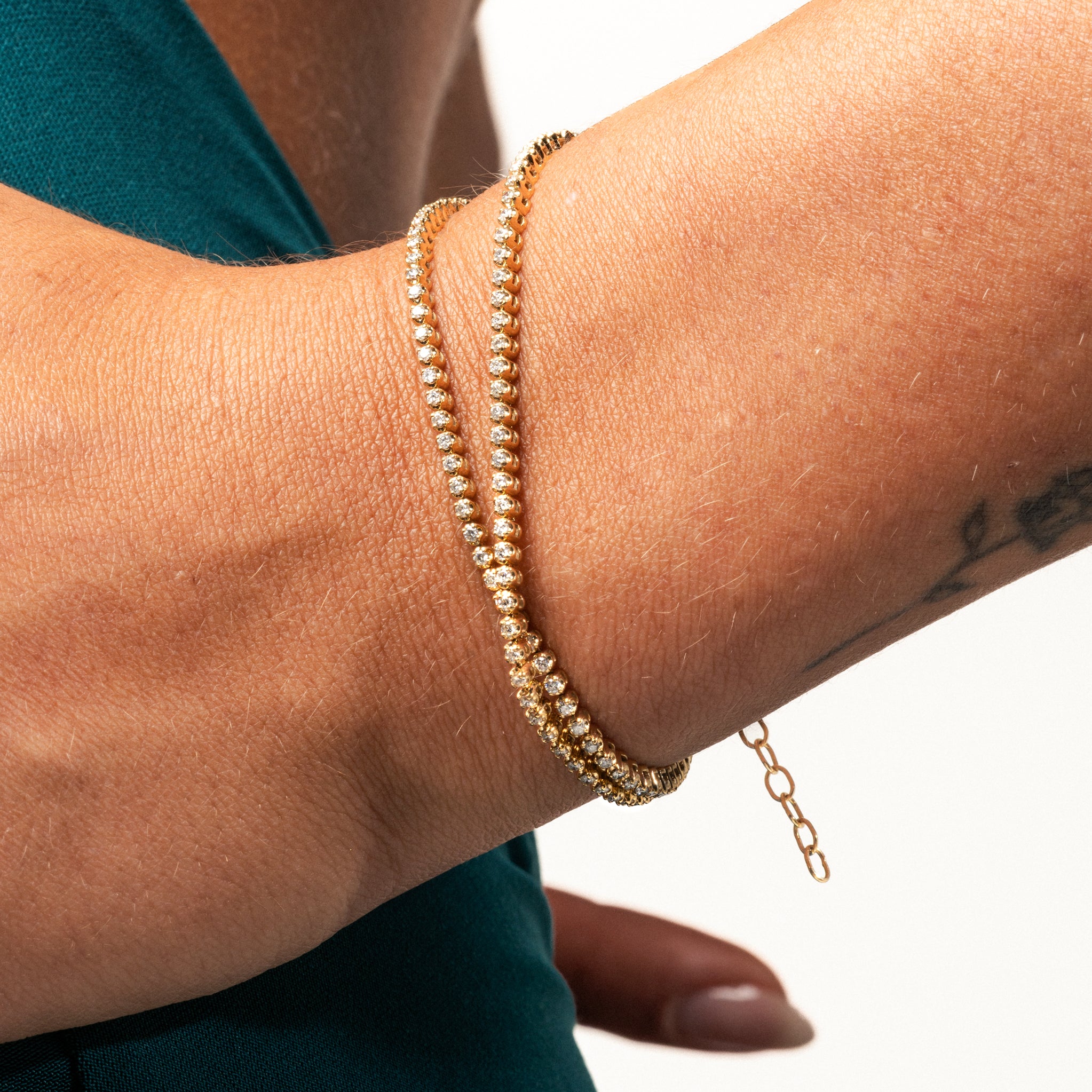 Close up of a hand wearing a Maia certified diamond necklace styled as a wrap bracelet on a gold chain.