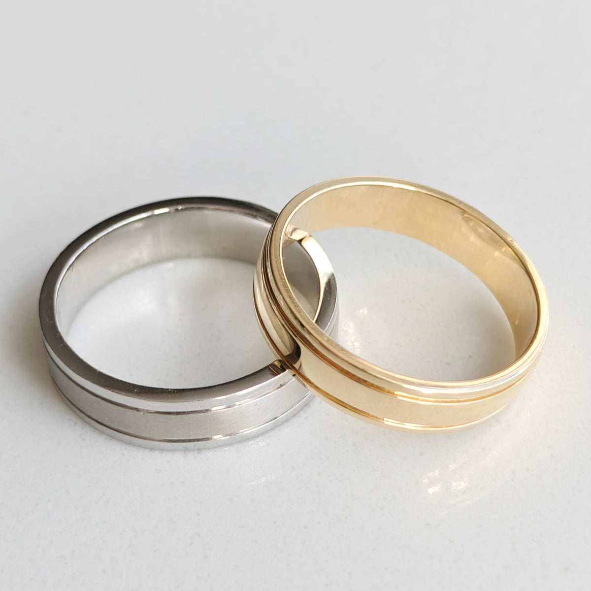 Two groove detail wedding rings, one silver with polished lines and one gold, showcasing modern design and elegance.