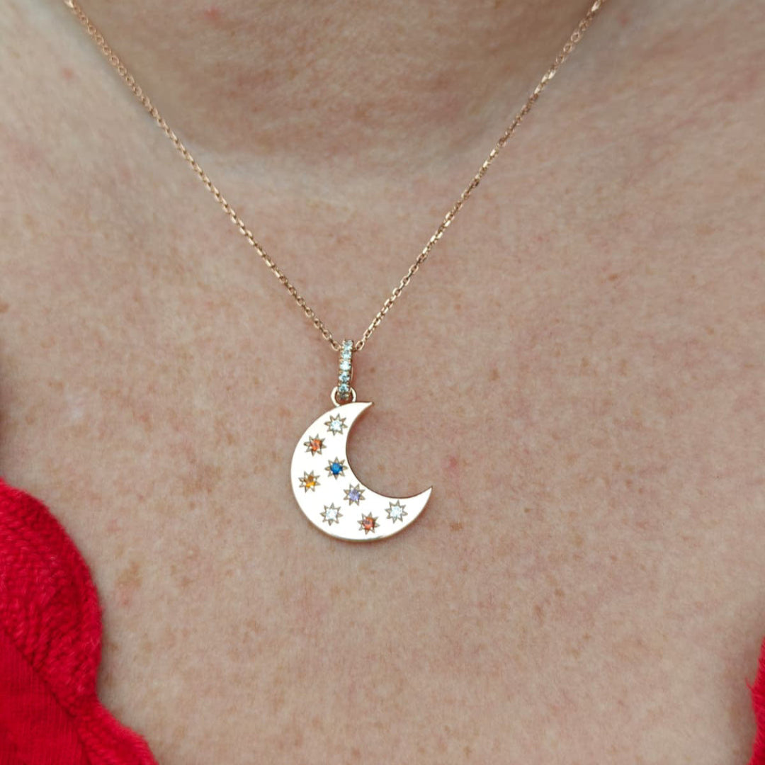Necklace with a crescent moon pendant featuring stars and colorful gemstones on a person's neck.